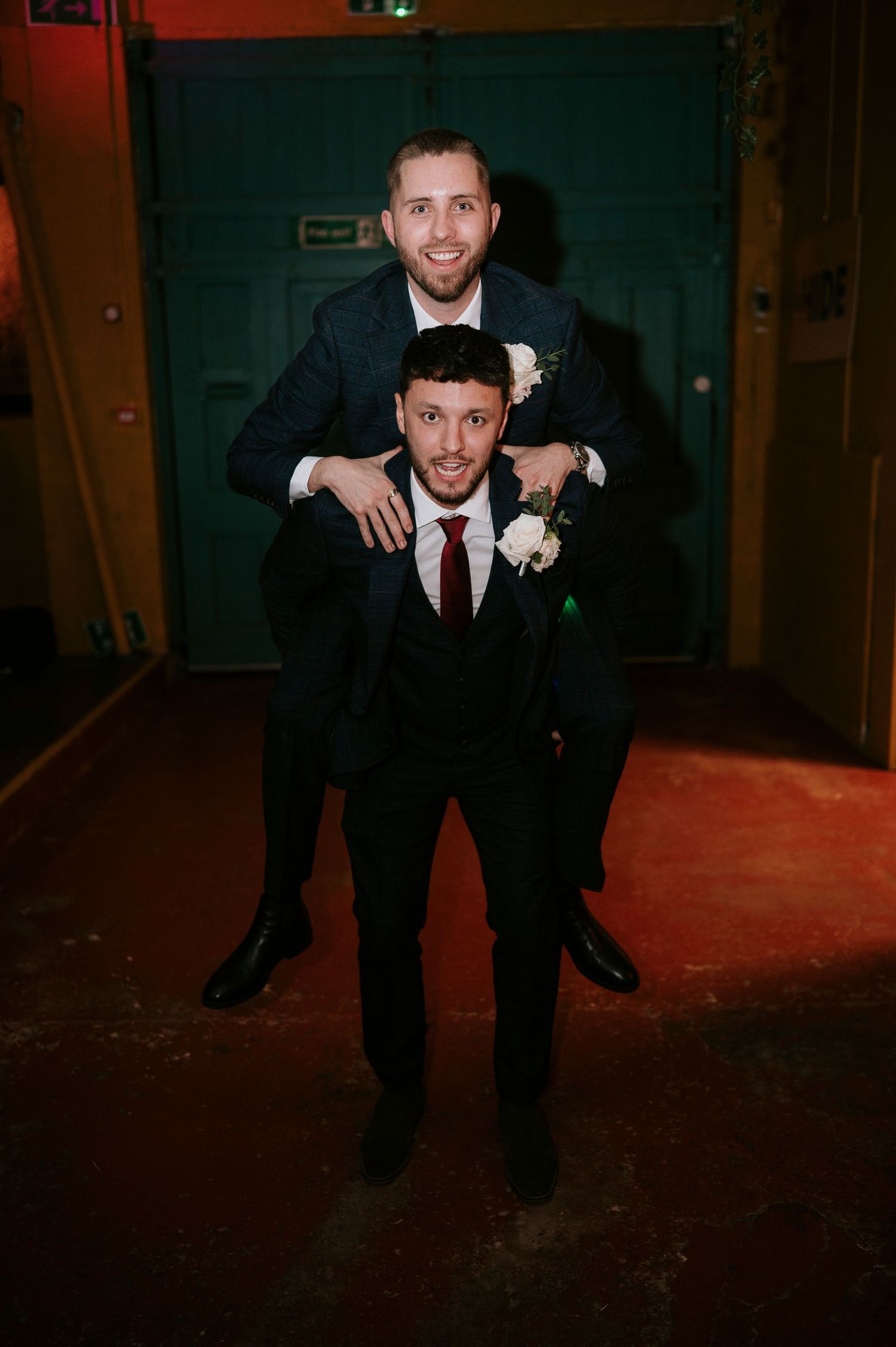 Two groomsmen share a fun piggyback pose at the wedding reception venue.