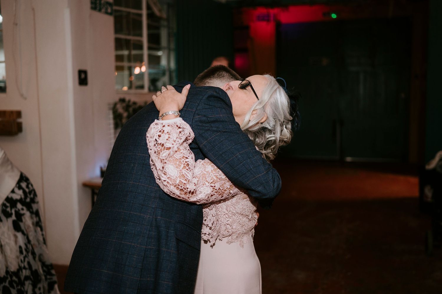 Couple sharing an emotional hug on the dance floor at a wedding reception in a warmly lit venue.