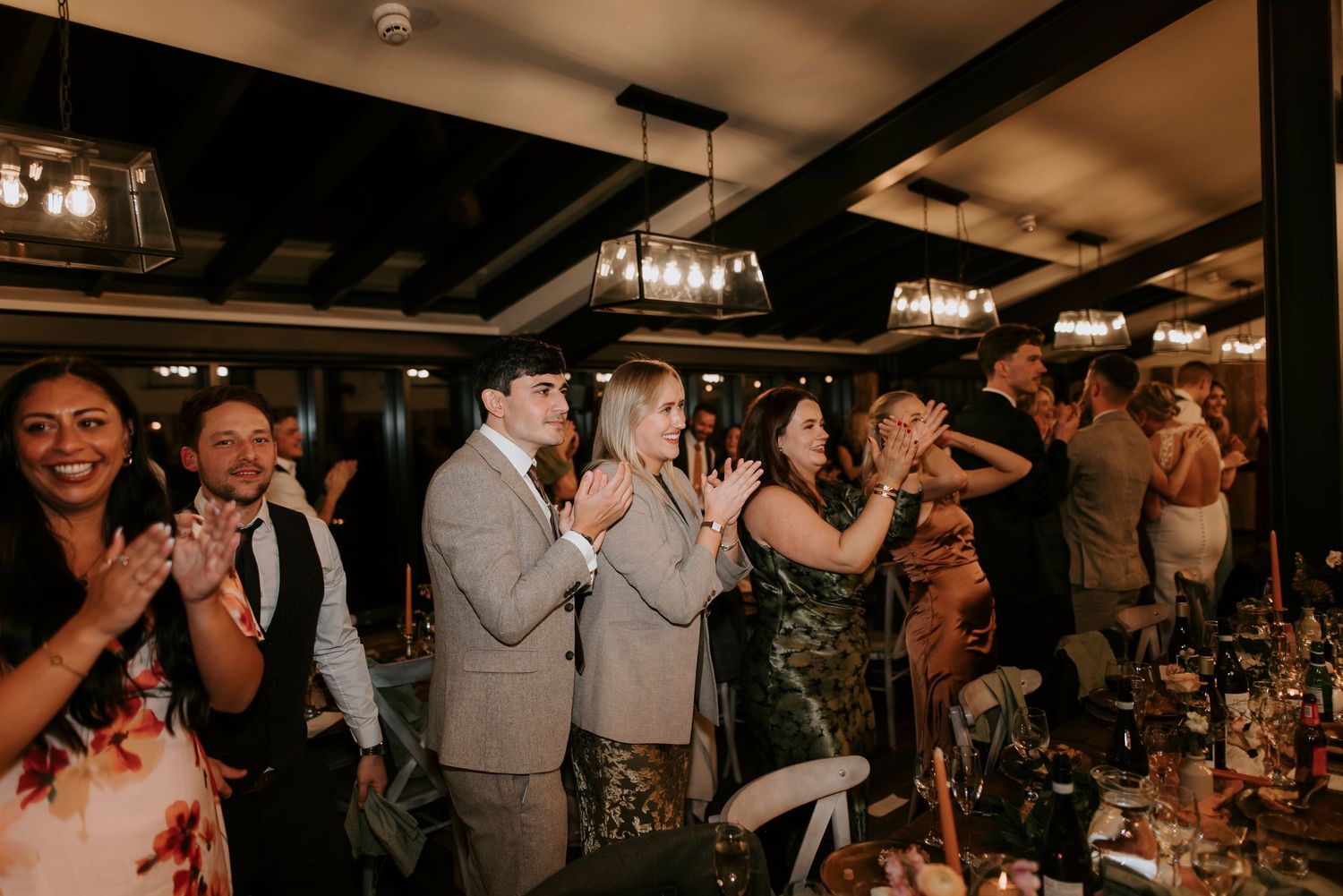 Wedding guests dance and celebrate together on a dimly lit dance floor during a reception party.