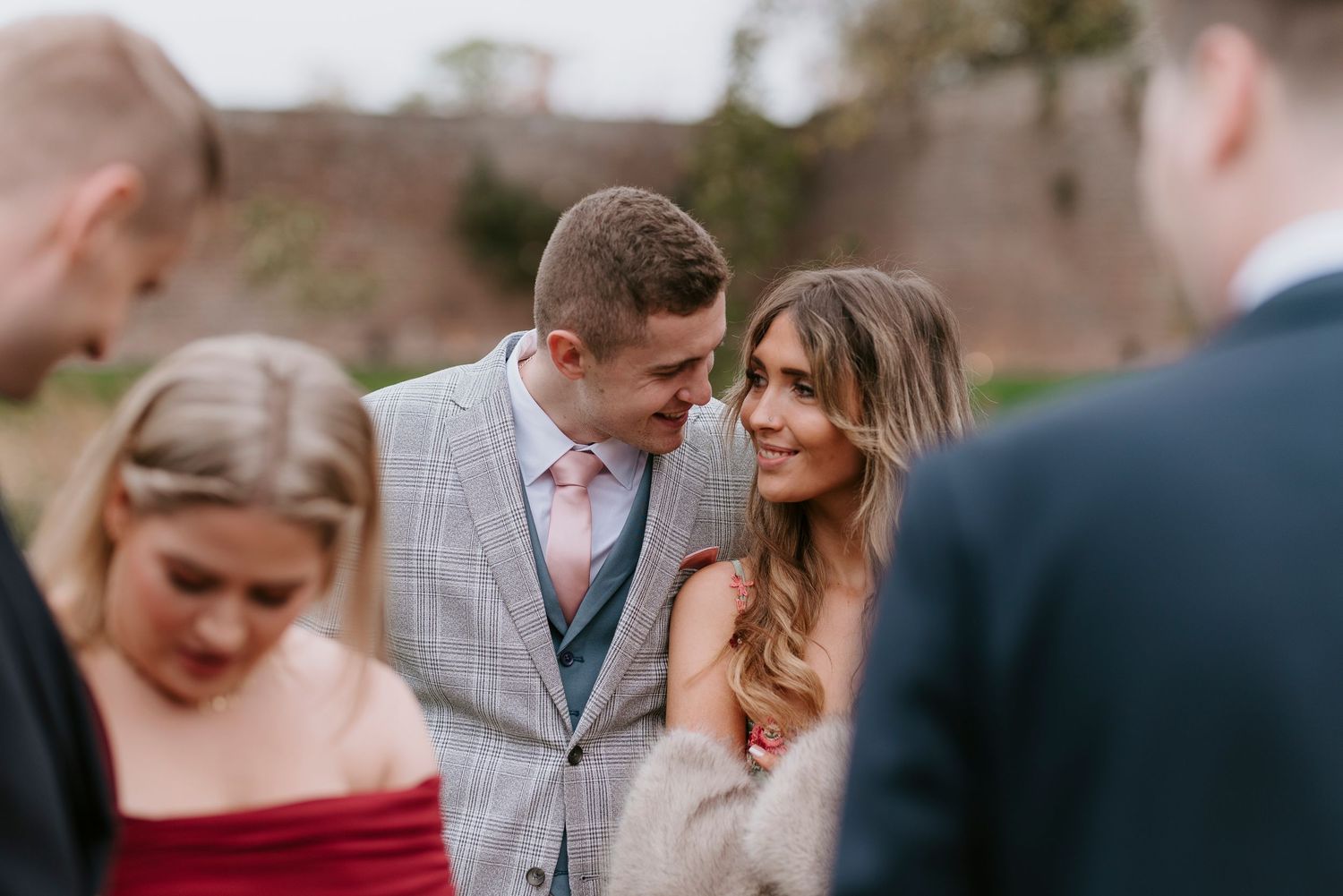 A couple shares a tender moment during an outdoor wedding celebration with guests in the background.