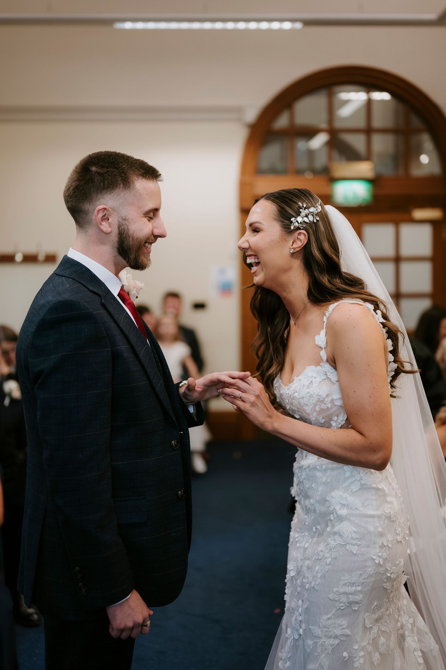Joyful bride and groom laugh together holding hands during wedding ceremony in elegant venue.