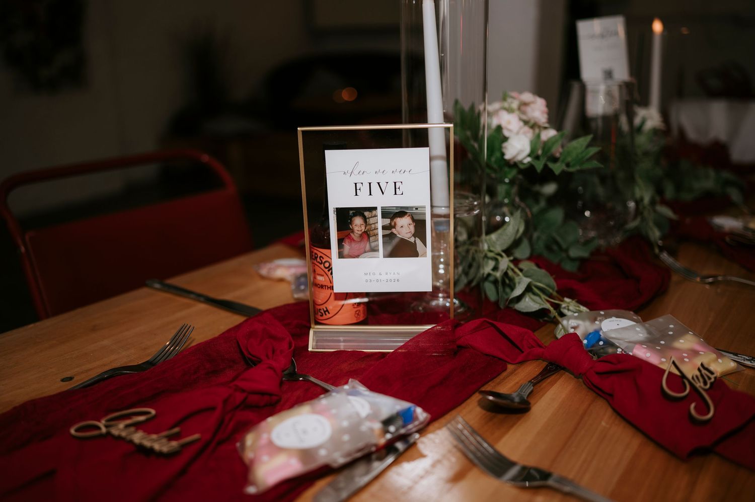 Wedding table number five display with couple photo, red velvet runners, candles, and floral centerpiece.