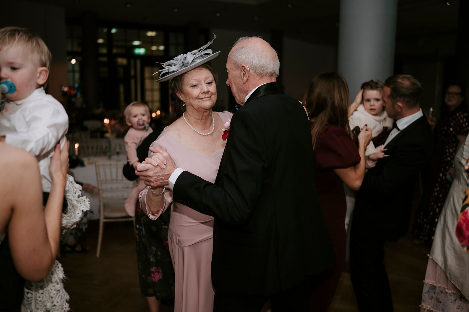 Wedding celebration with multiple couples dancing together on dimly lit dance floor.