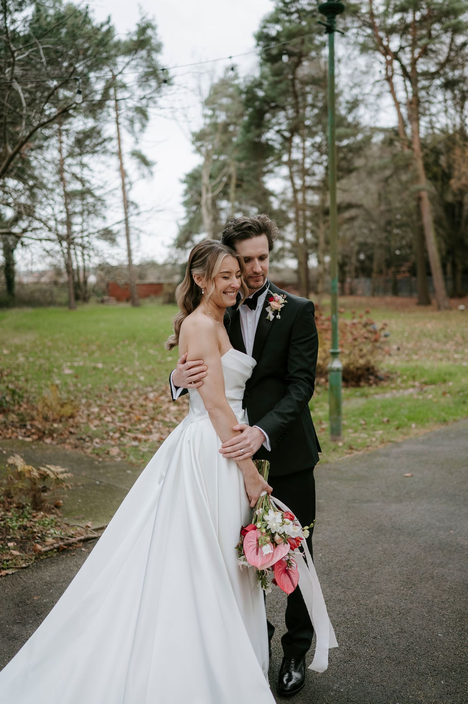 A couple shares joyful moments together outdoors in a wooded park setting during their wedding celebration.