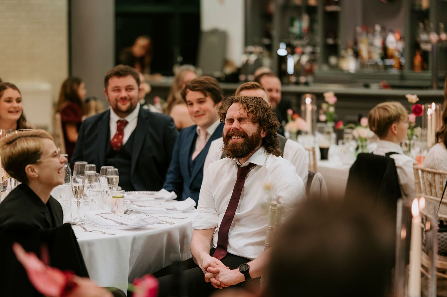 Wedding guests seated at round tables with white linens enjoy a reception dinner in an elegant indoor venue.
