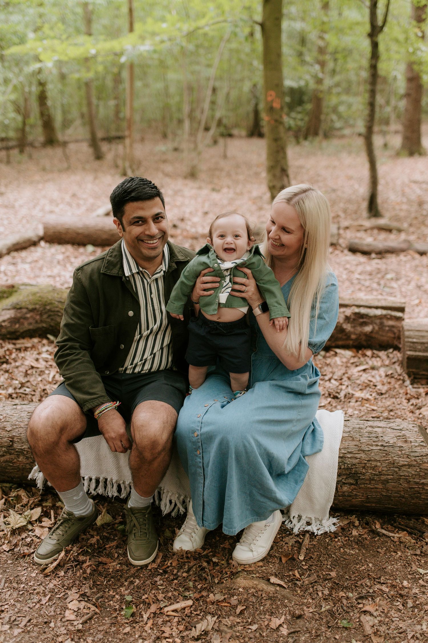 A family sitting together on a fallen log in a wooded forest setting during an outdoor photo session.