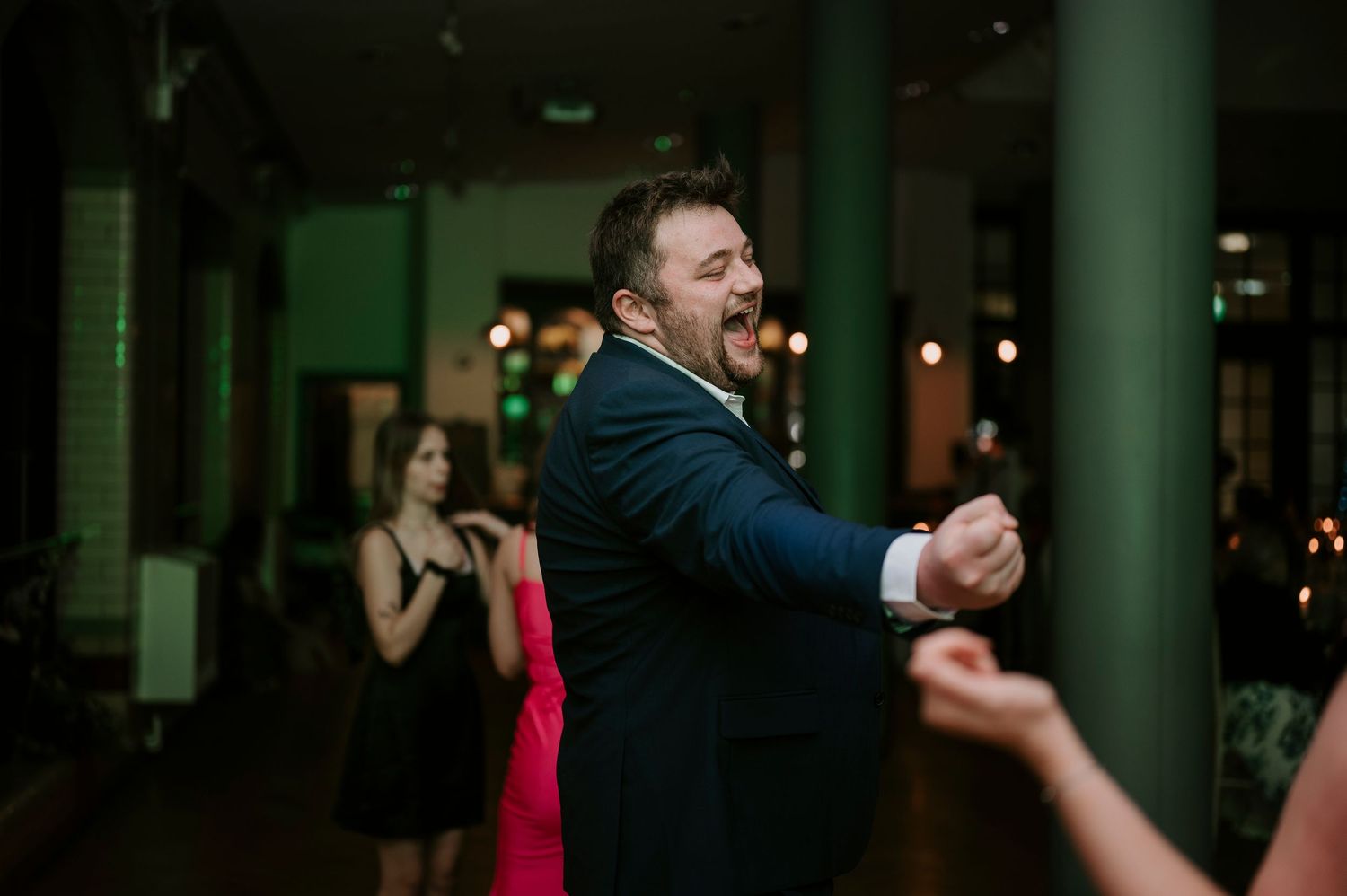 Wedding guests dancing and celebrating in a modern venue with columns.