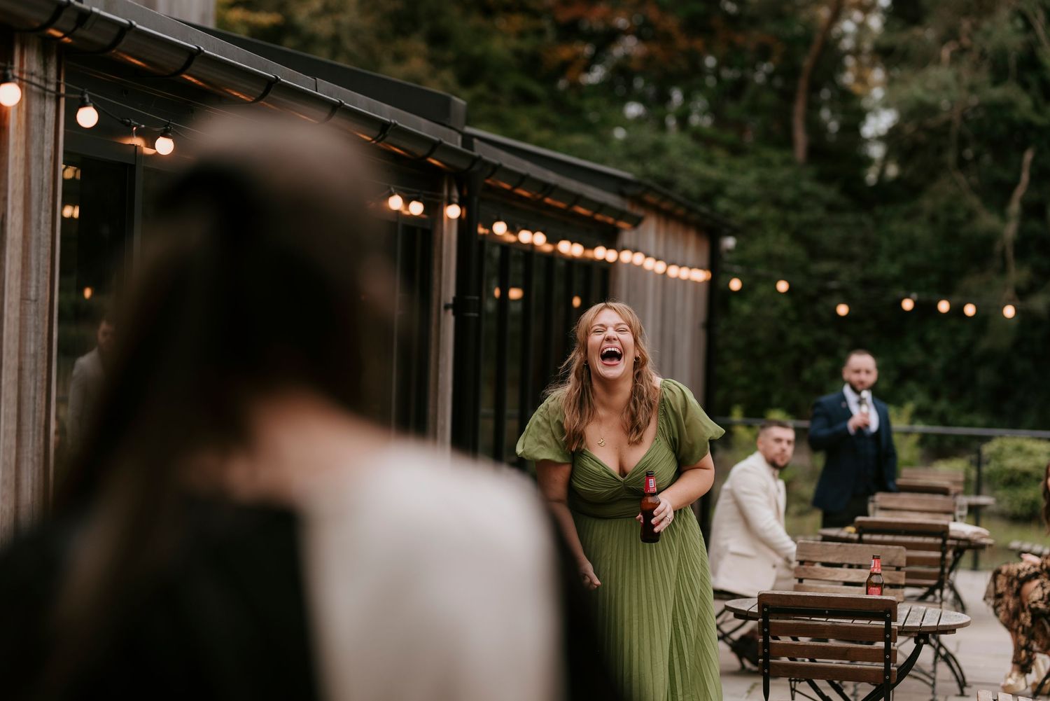 Outdoor event venue decorated with string lights and wooden chairs while guests enjoy a lively evening celebration.