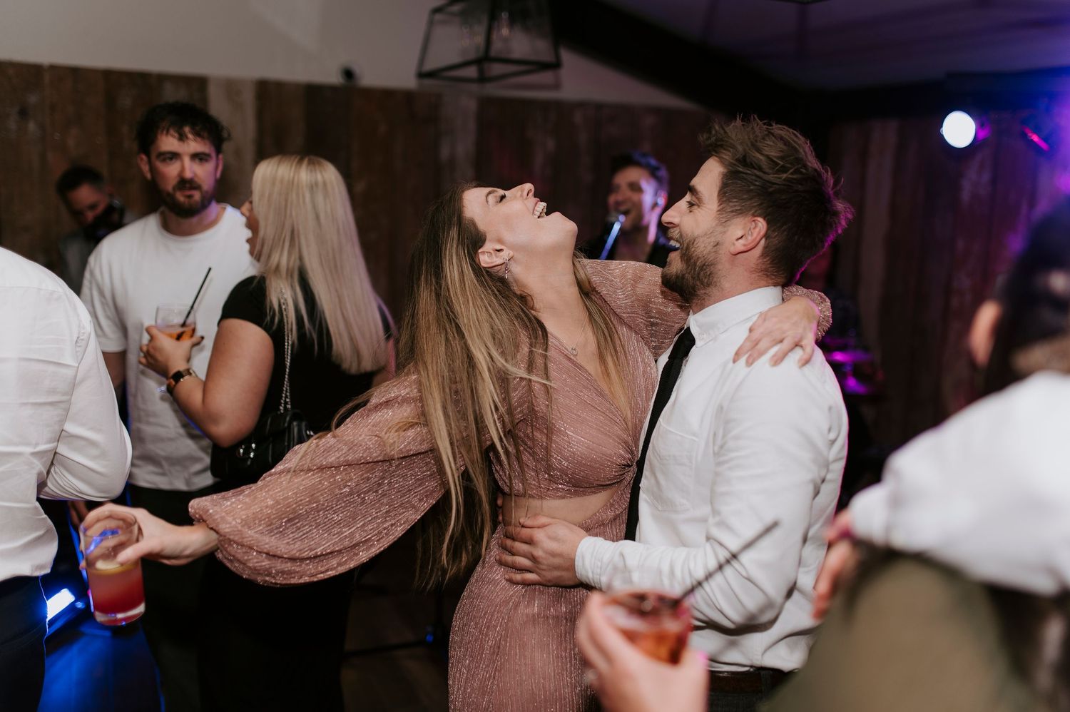 Couples dancing and embracing on a dimly lit dance floor at a party or celebration.