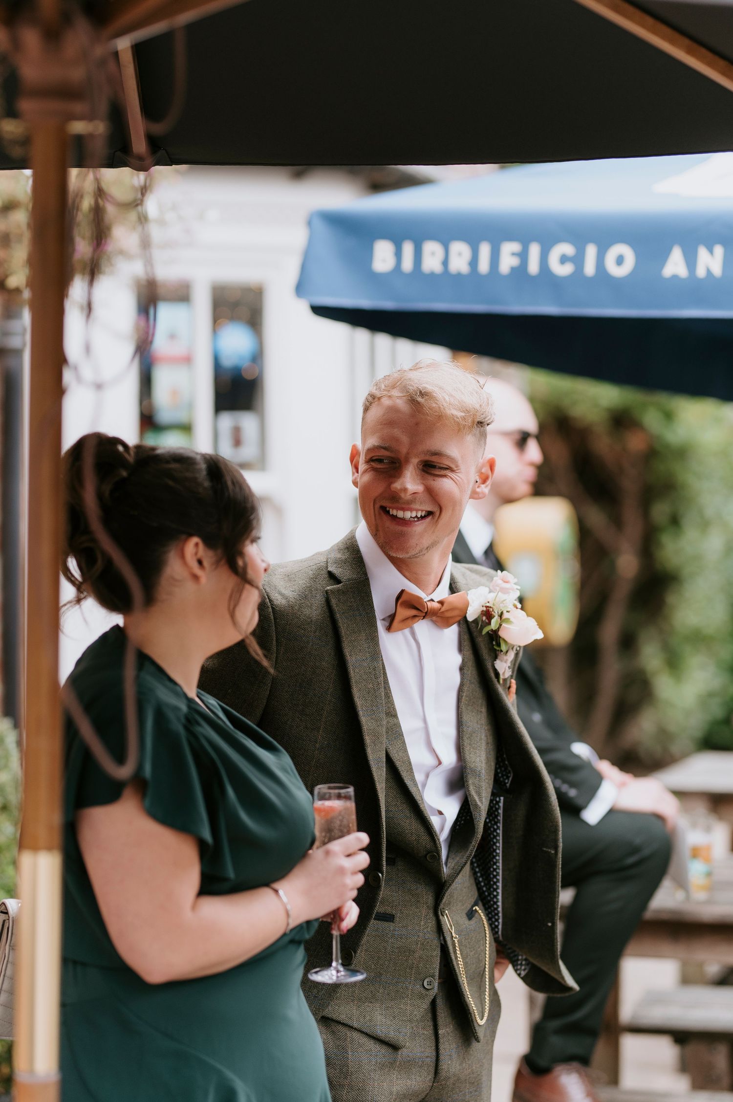 A group of wedding guests laugh and socialize while holding wine glasses on an outdoor patio.