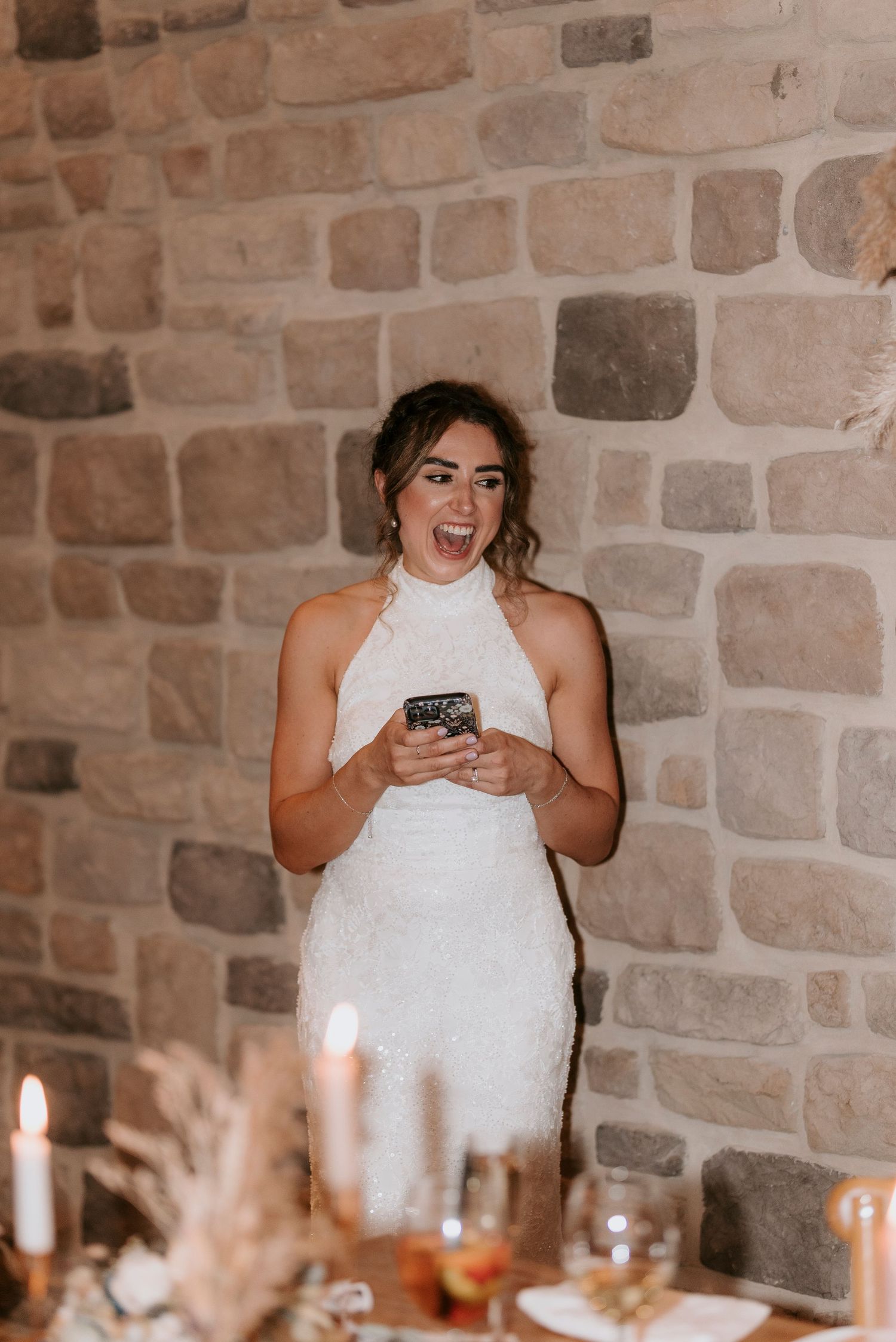 A sequence of emotional reactions in a white dress against a stone wall during a wedding reception.
