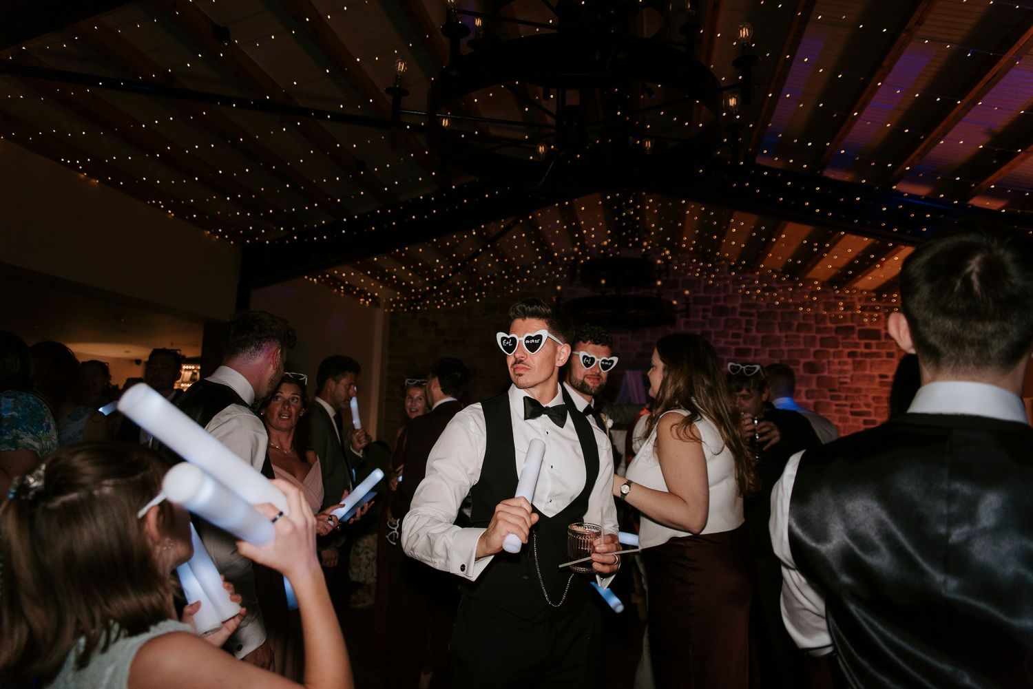 Wedding guests dance and celebrate on a dimly lit dance floor during a reception party.