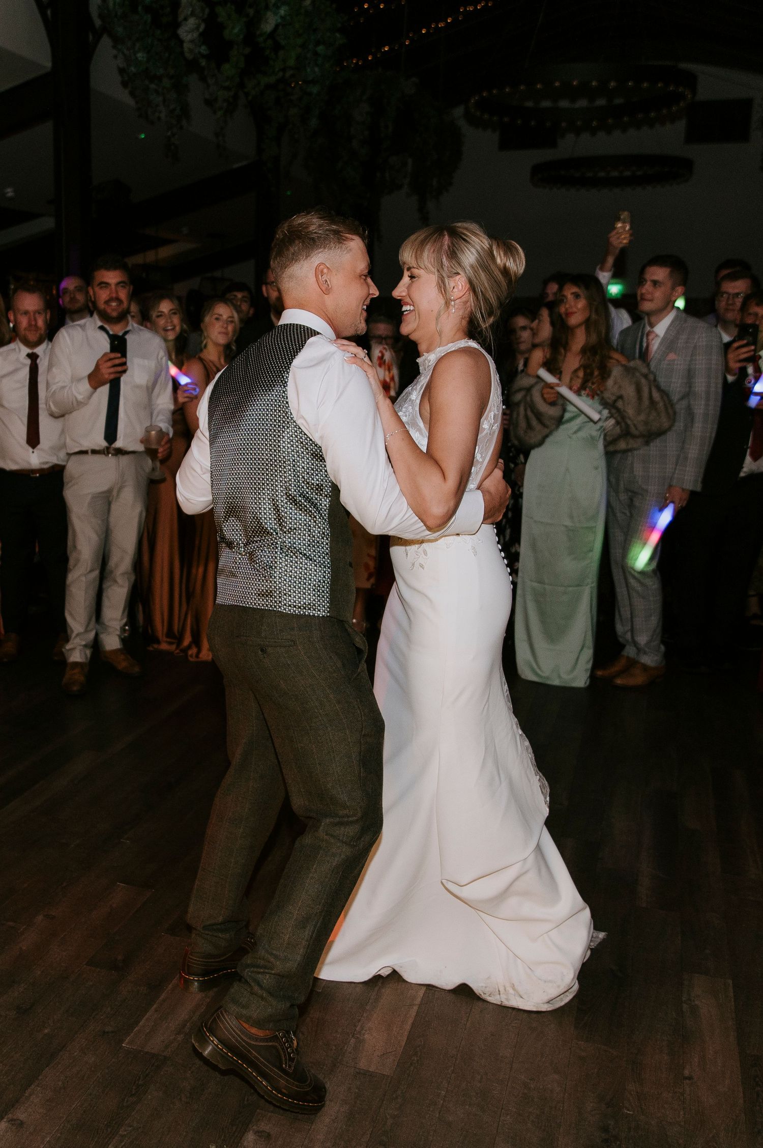 A couple dances together at a wedding reception on a wooden dance floor surrounded by guests.