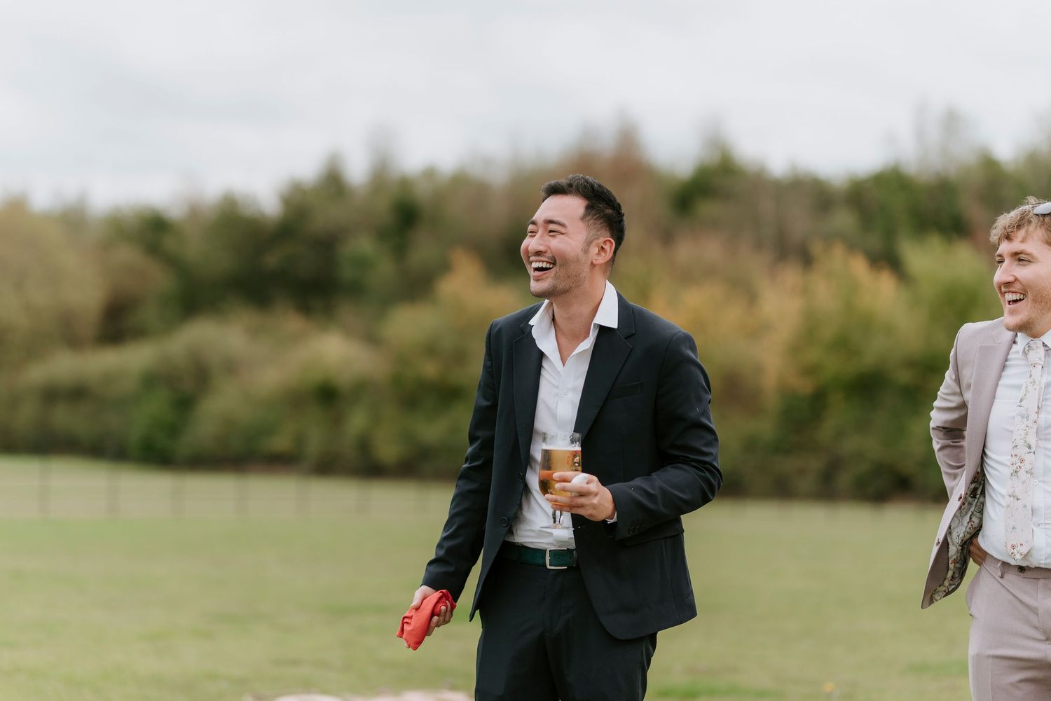 A joyful wedding moment captured outdoors with laughter and celebration in a green field setting.