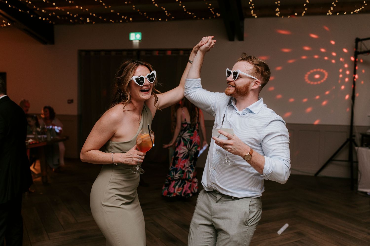 Couple dancing and laughing together at a dimly lit wedding reception with red lighting effects in background.