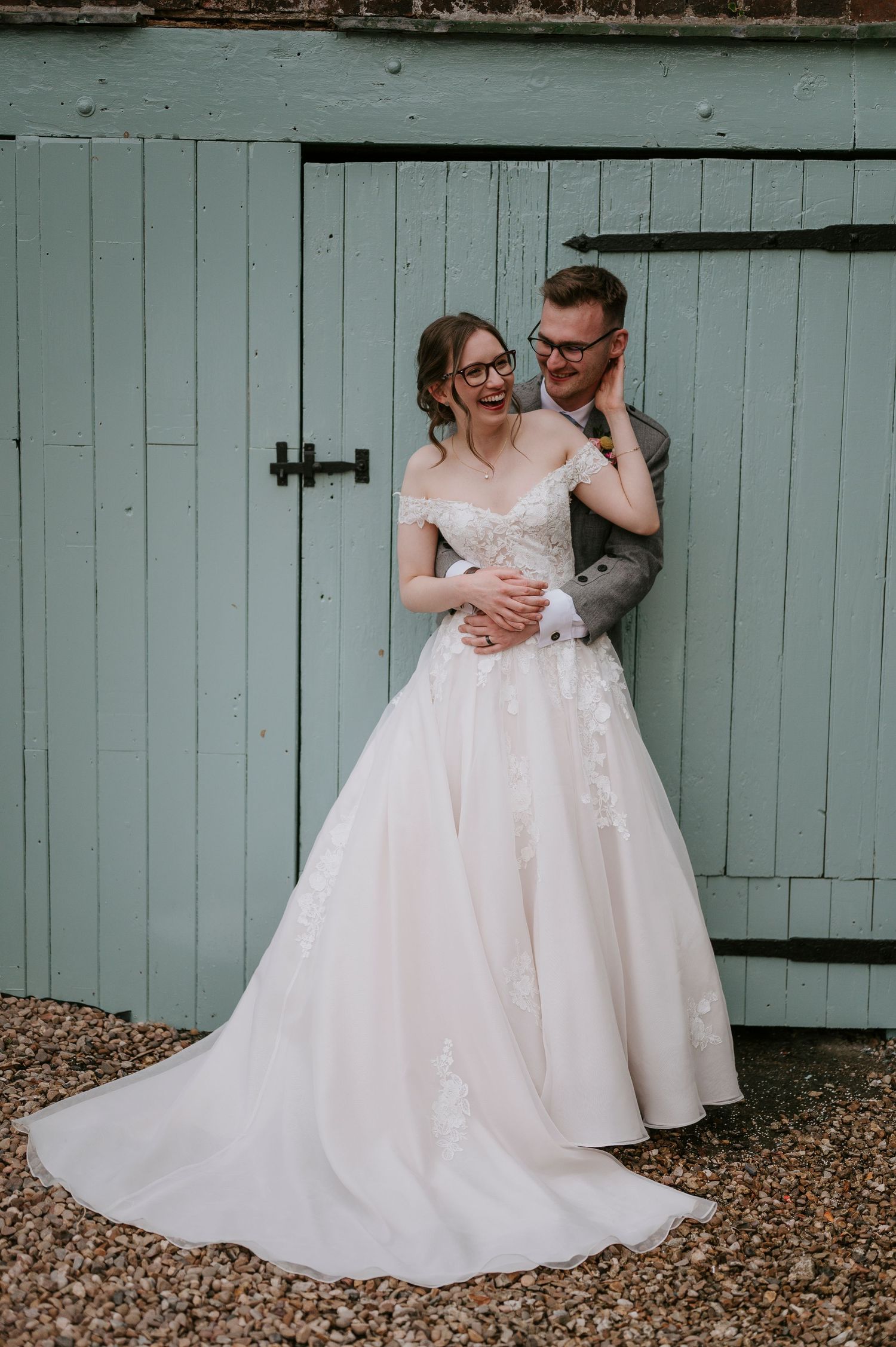A romantic wedding couple embraces in front of a mint green barn door on their special day.