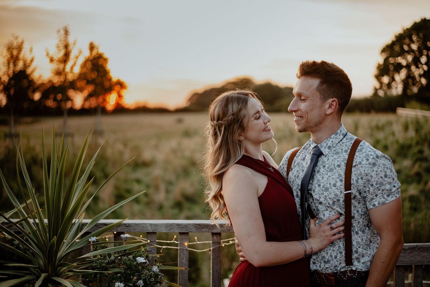 A couple shares a romantic moment at sunset in a field with yucca plants and warm golden lighting.