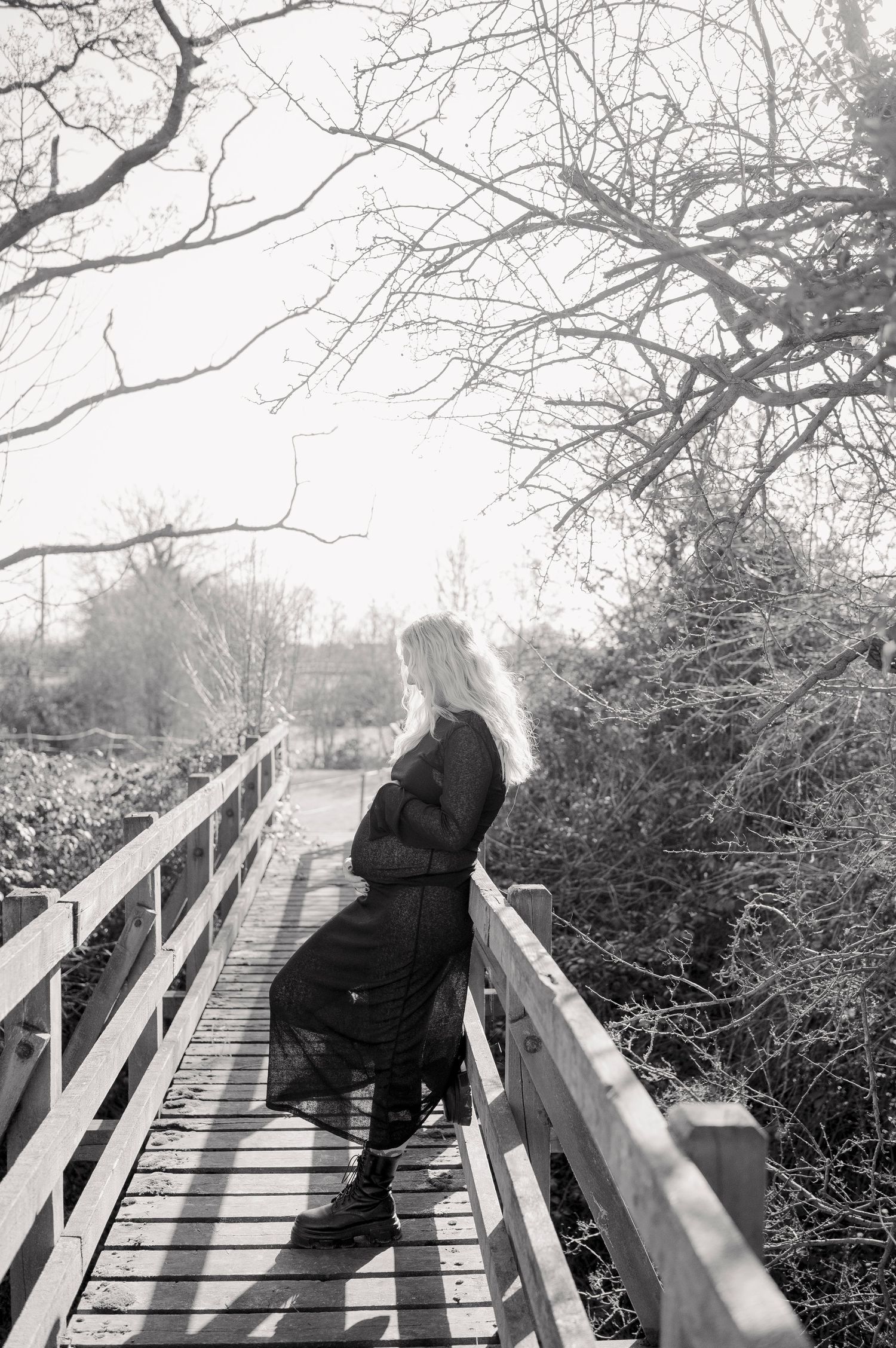 Black and white photo of a wooden boardwalk through bare winter trees creating dramatic shadows.