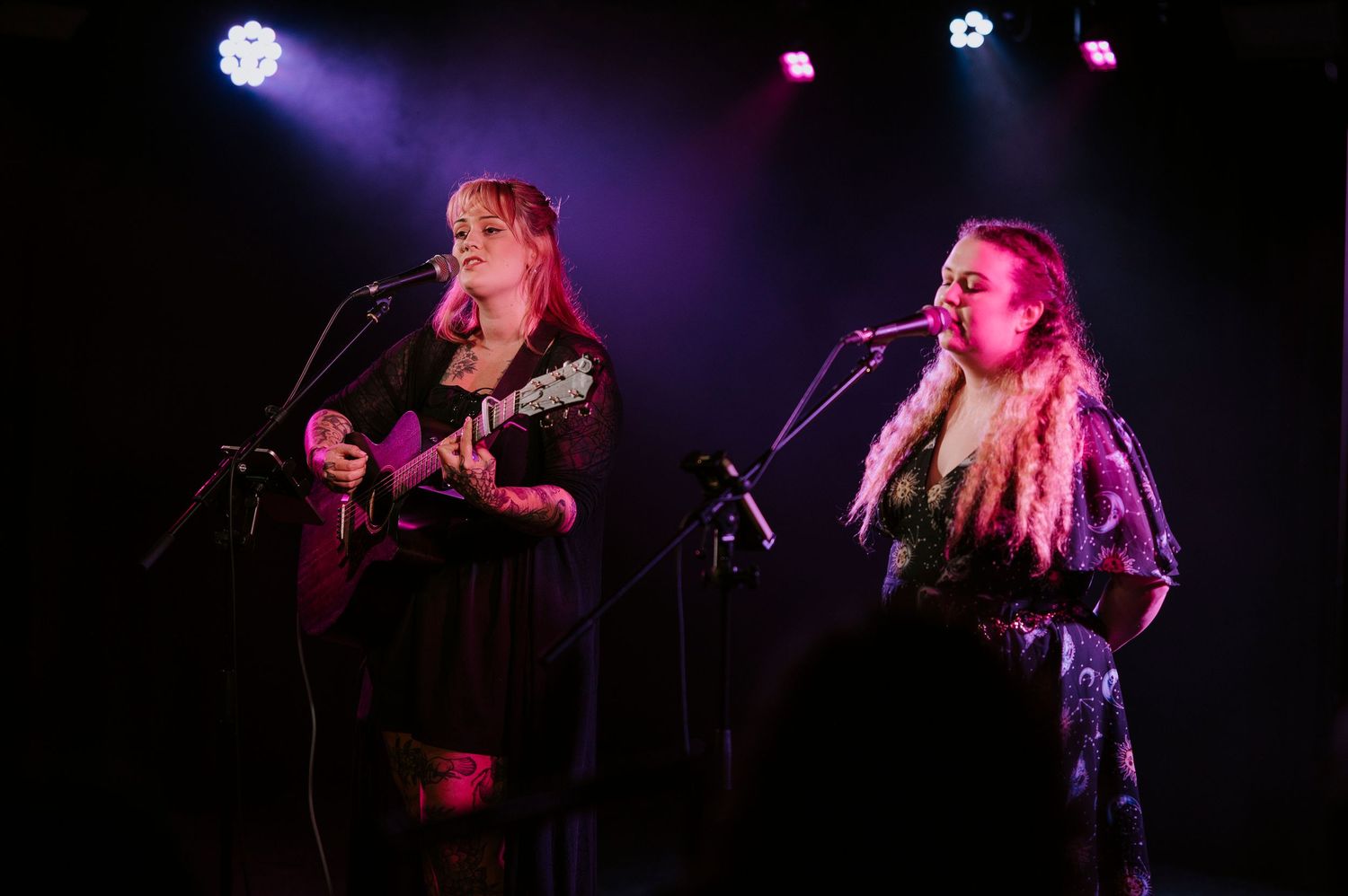 Musicians perform on a dark stage with purple lighting during a live concert performance.