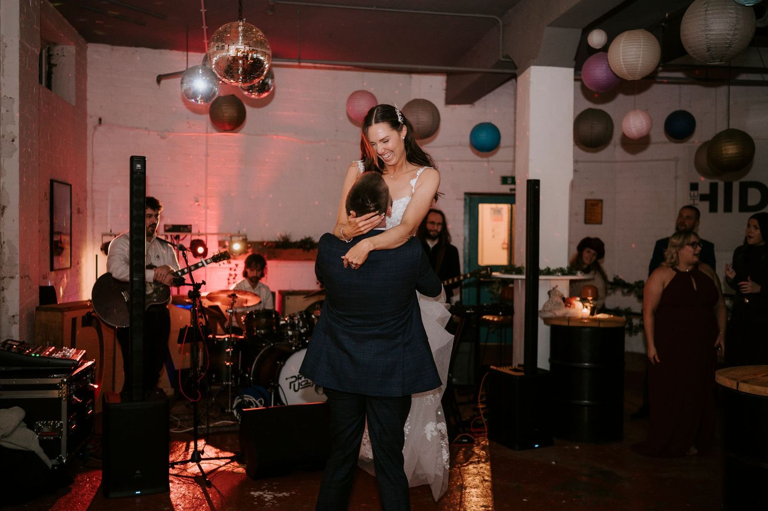 Bride and groom share romantic first dance at wedding reception with live band and colorful paper lanterns.