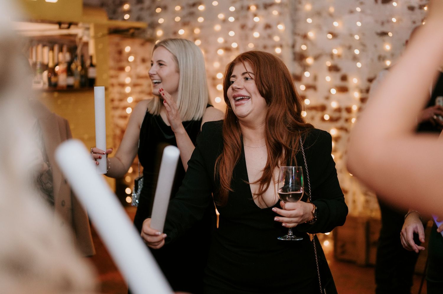 Two women laugh and smile joyfully while holding candles at a wedding reception.