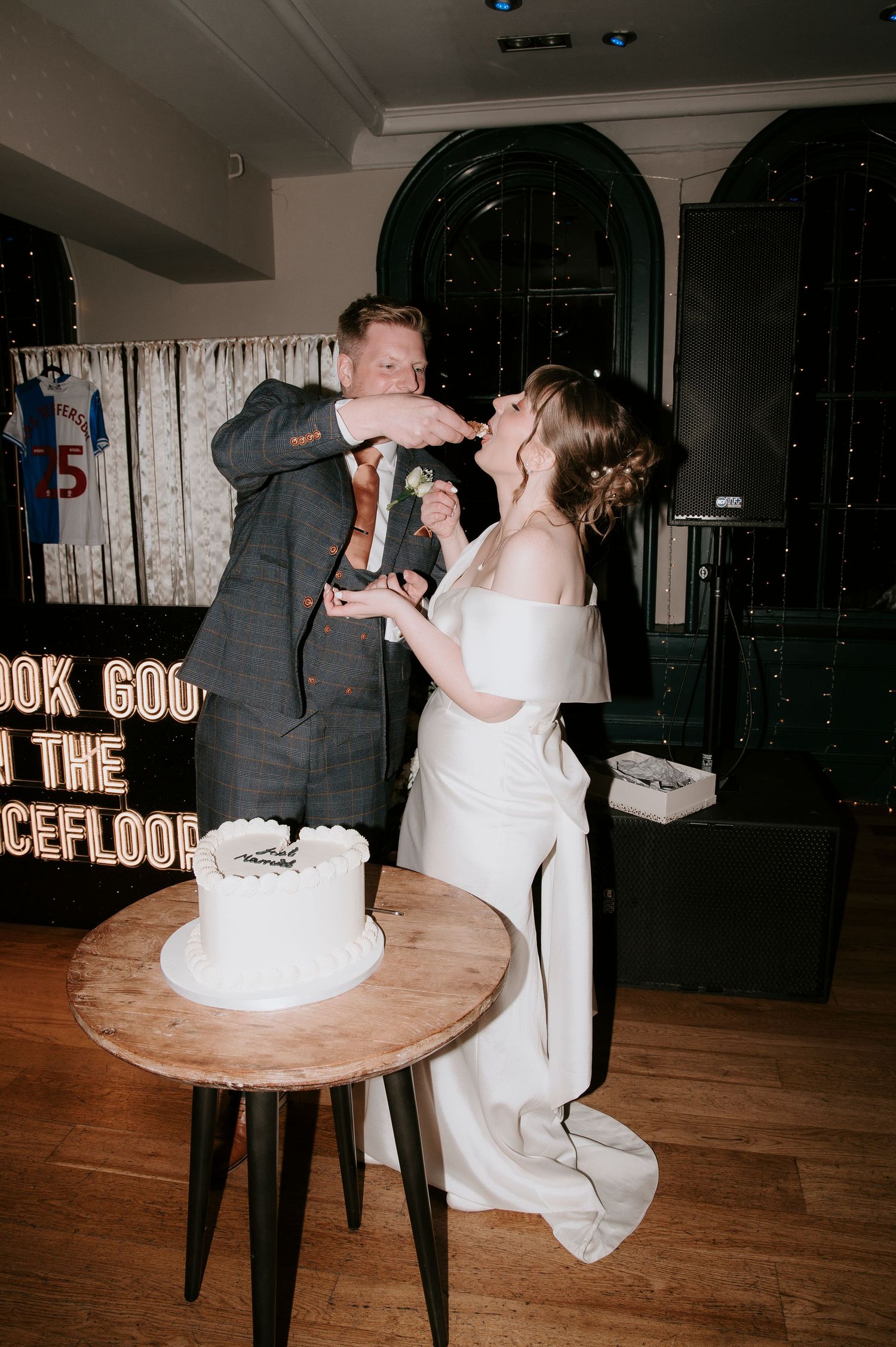 A couple in formal wedding attire dances together on a wooden floor during their first dance at a reception venue.
