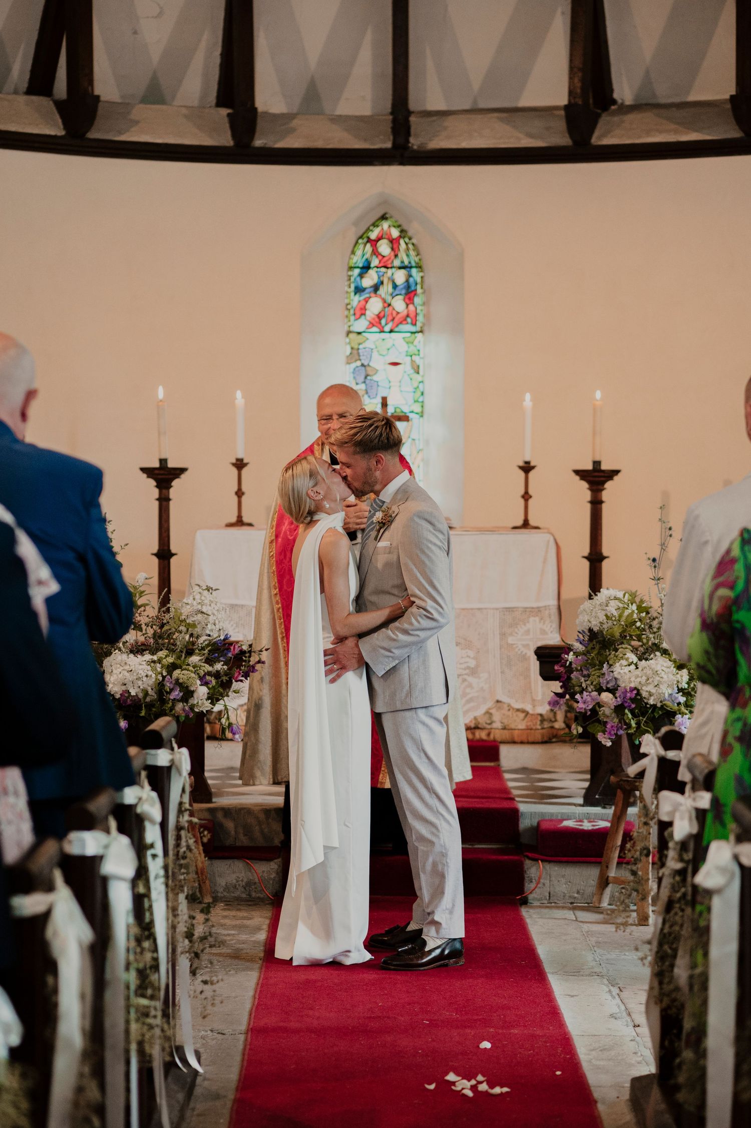 Intimate church wedding ceremony with stained glass windows and floral arrangements along the aisle.