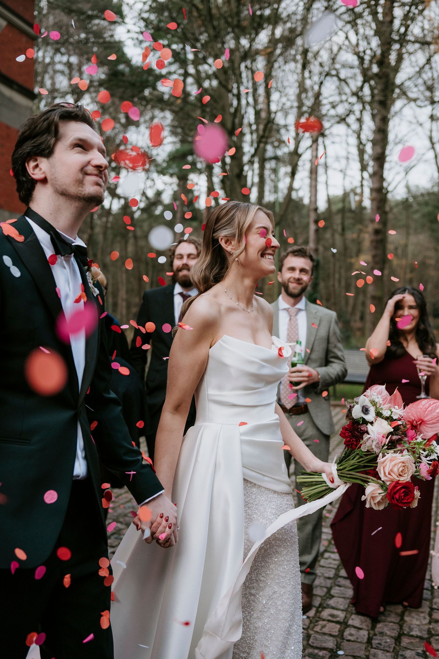 Wedding celebration with pink and red rose petals falling as guests gather outdoors.