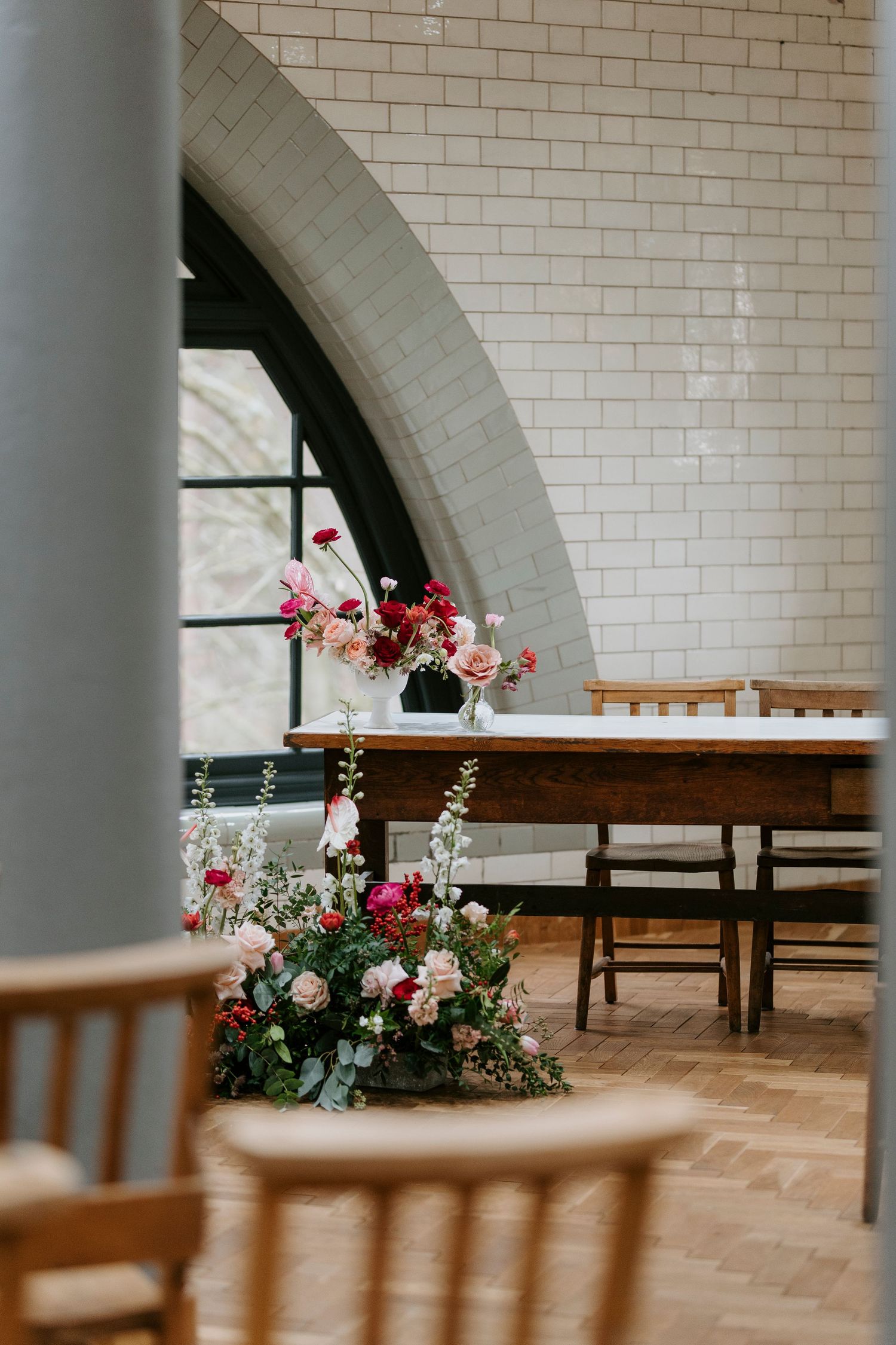 Wedding venue interior with arched white brick walls and floral arrangements decorating wooden benches.