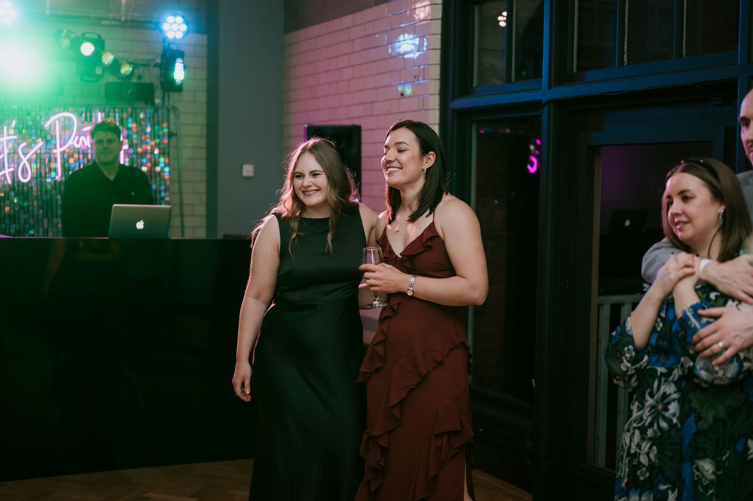Guests enjoy dancing under colorful lighting at indoor wedding reception venue.