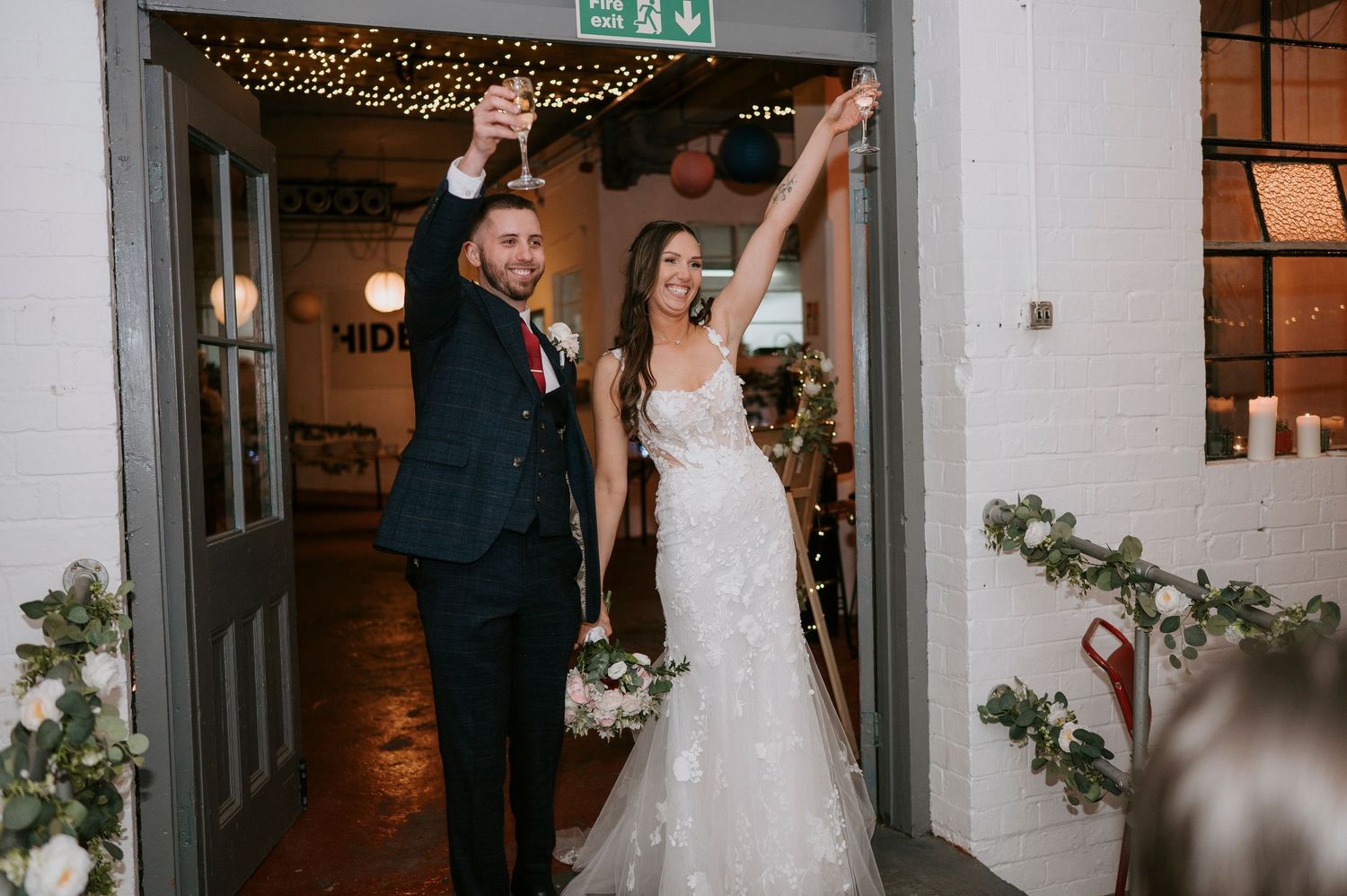 Wedding reception venue with twinkling string lights and white floral decorations along the walls.