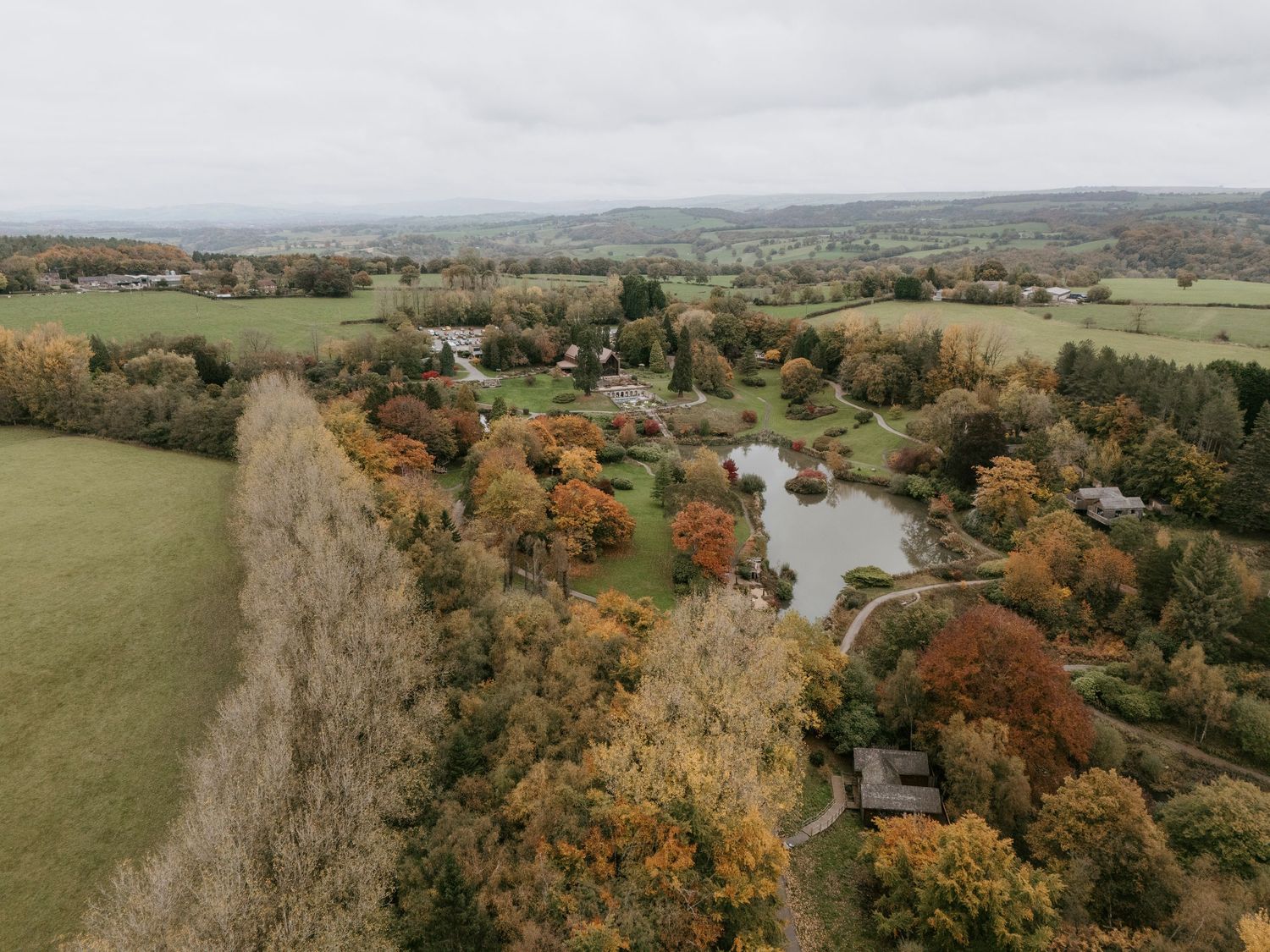 Aerial panoramic view of rolling hills and farmland with vibrant autumn foliage and a winding river in the valley.
