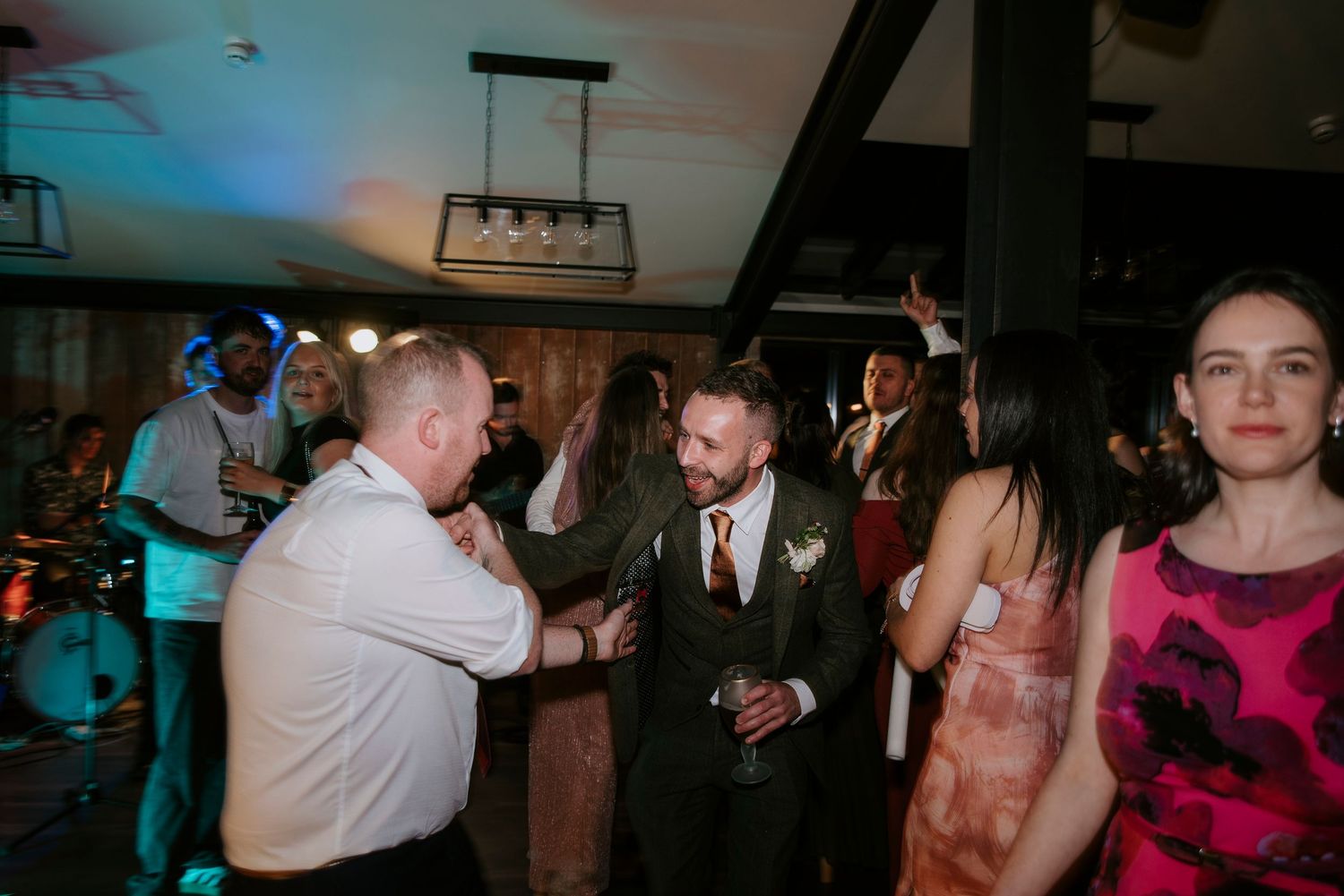 Wedding guests dance and celebrate on a dimly lit dance floor with blue lighting at a reception party.