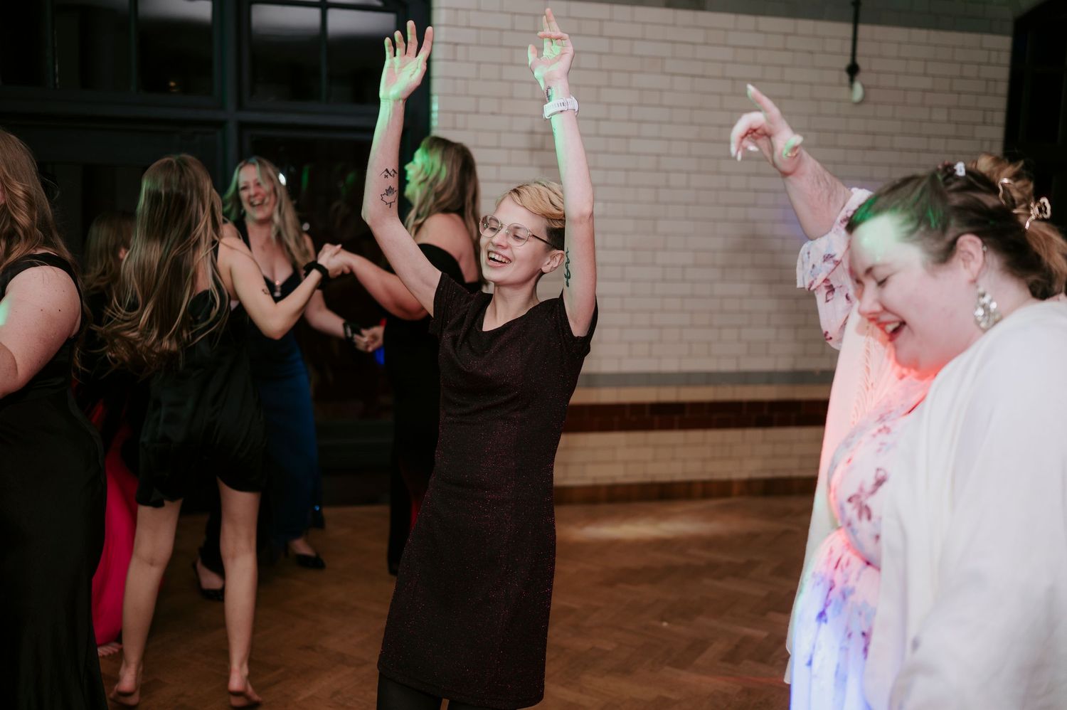 Wedding guests dancing and celebrating on a wooden dance floor under ambient lighting.