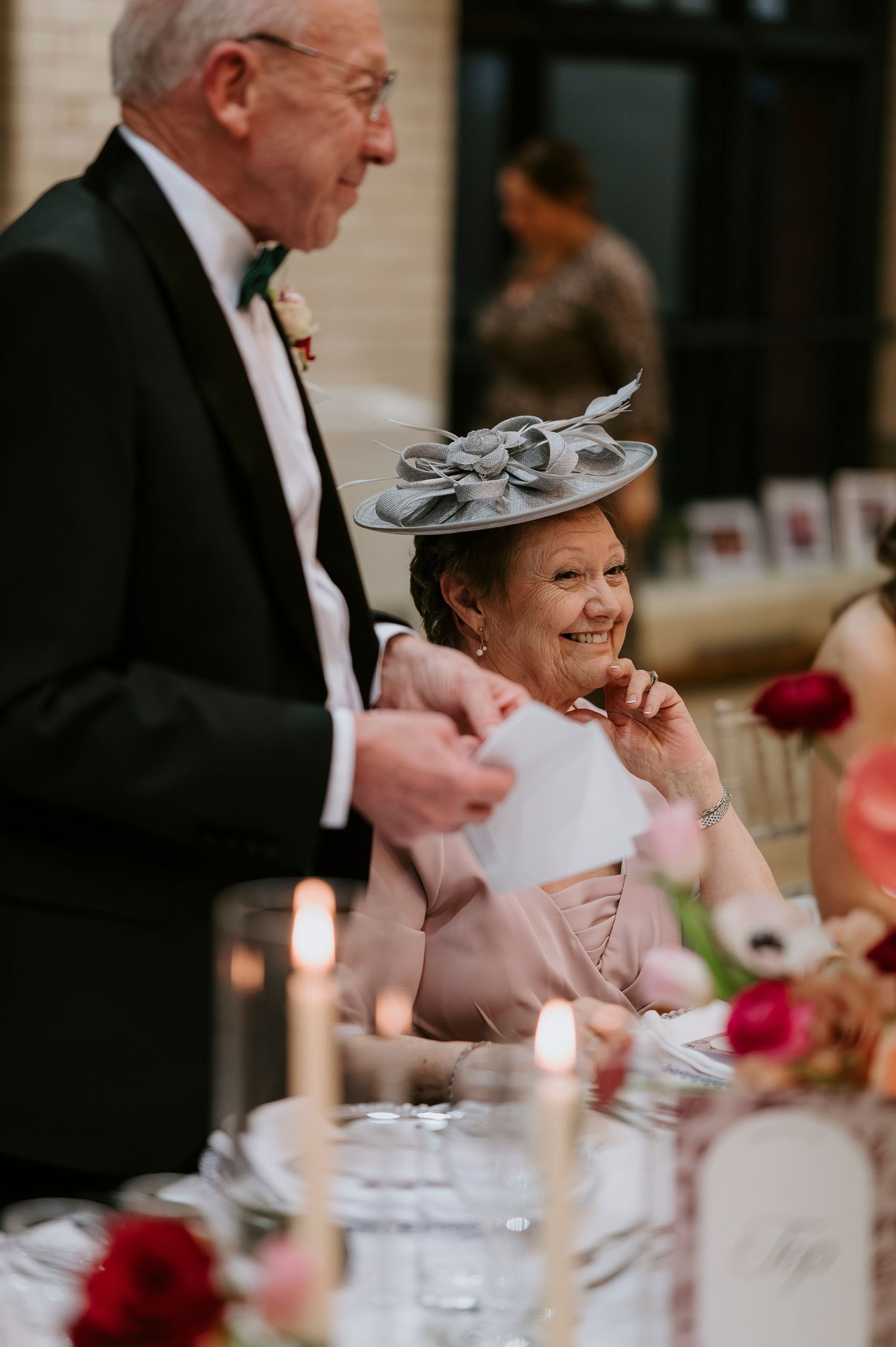 Formal dinner reception with guests seated at tables decorated with red flowers and candles.