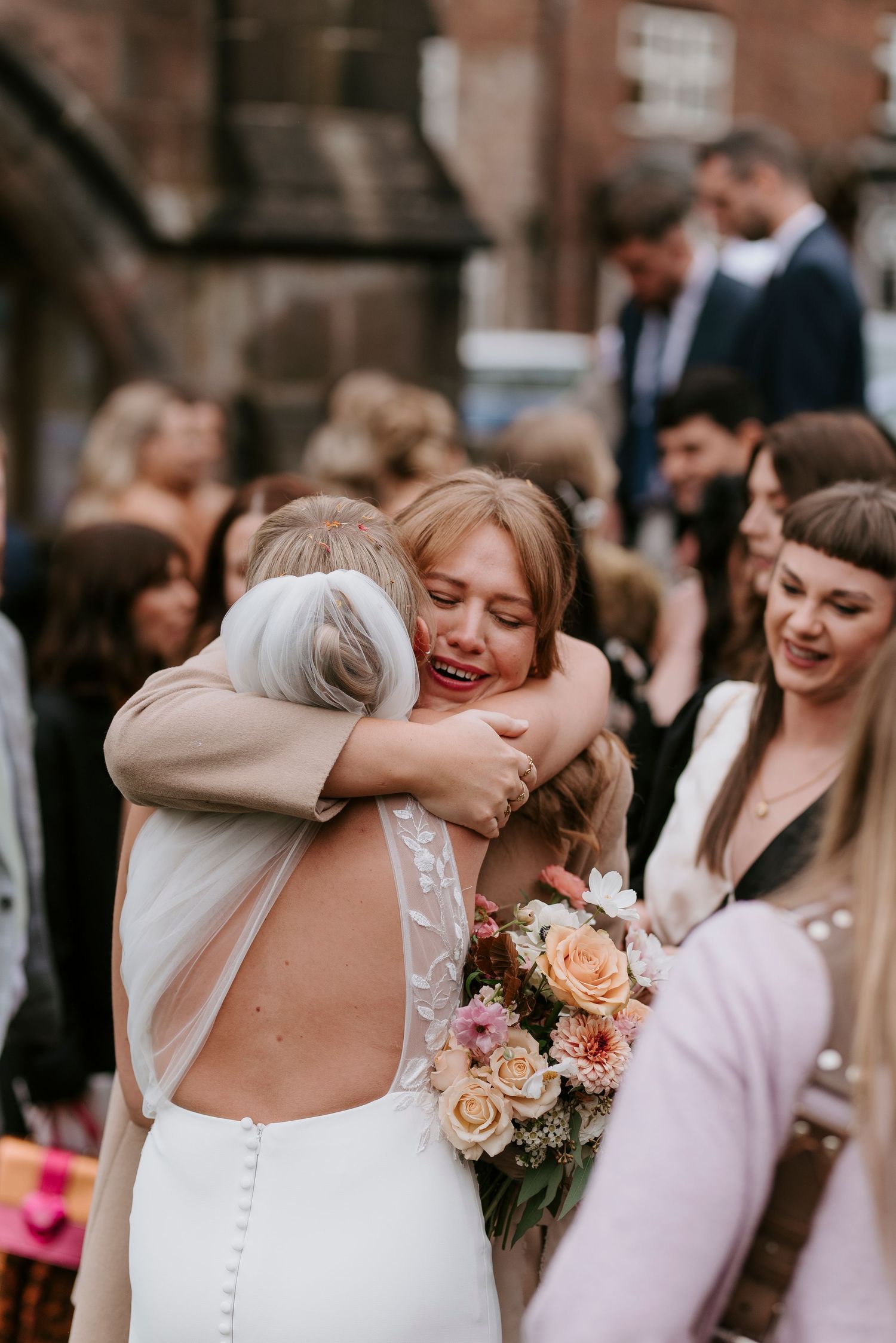An emotional embrace captured during a wedding celebration surrounded by guests and pink roses.