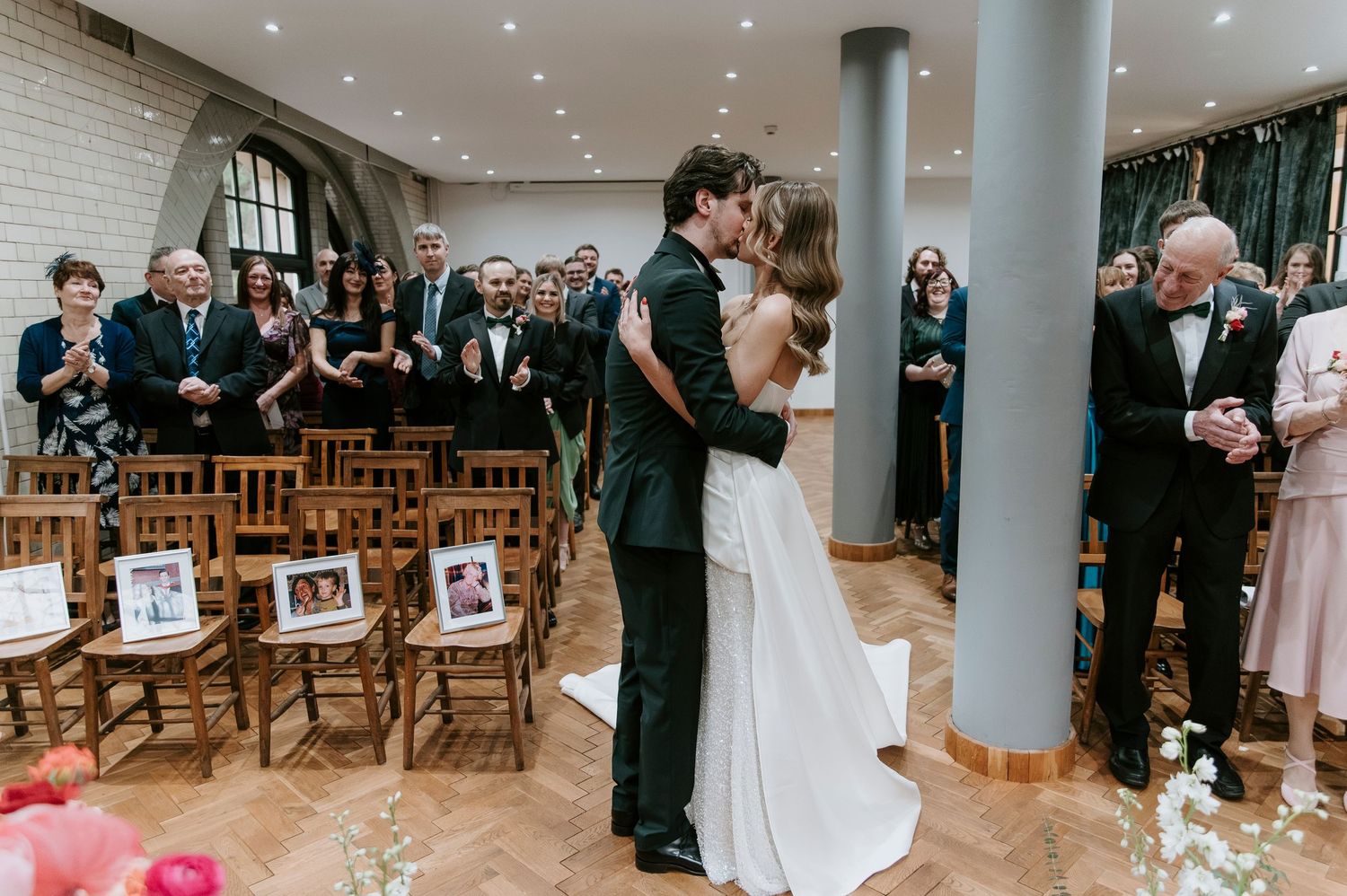 Wedding guests gather in an elegant venue with white brick walls and modern lighting for a celebration.
