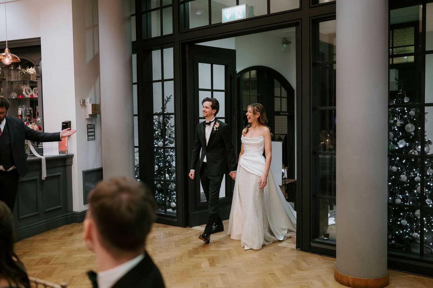 A couple shares their first dance in a modern venue with tall columns and dramatic lighting.