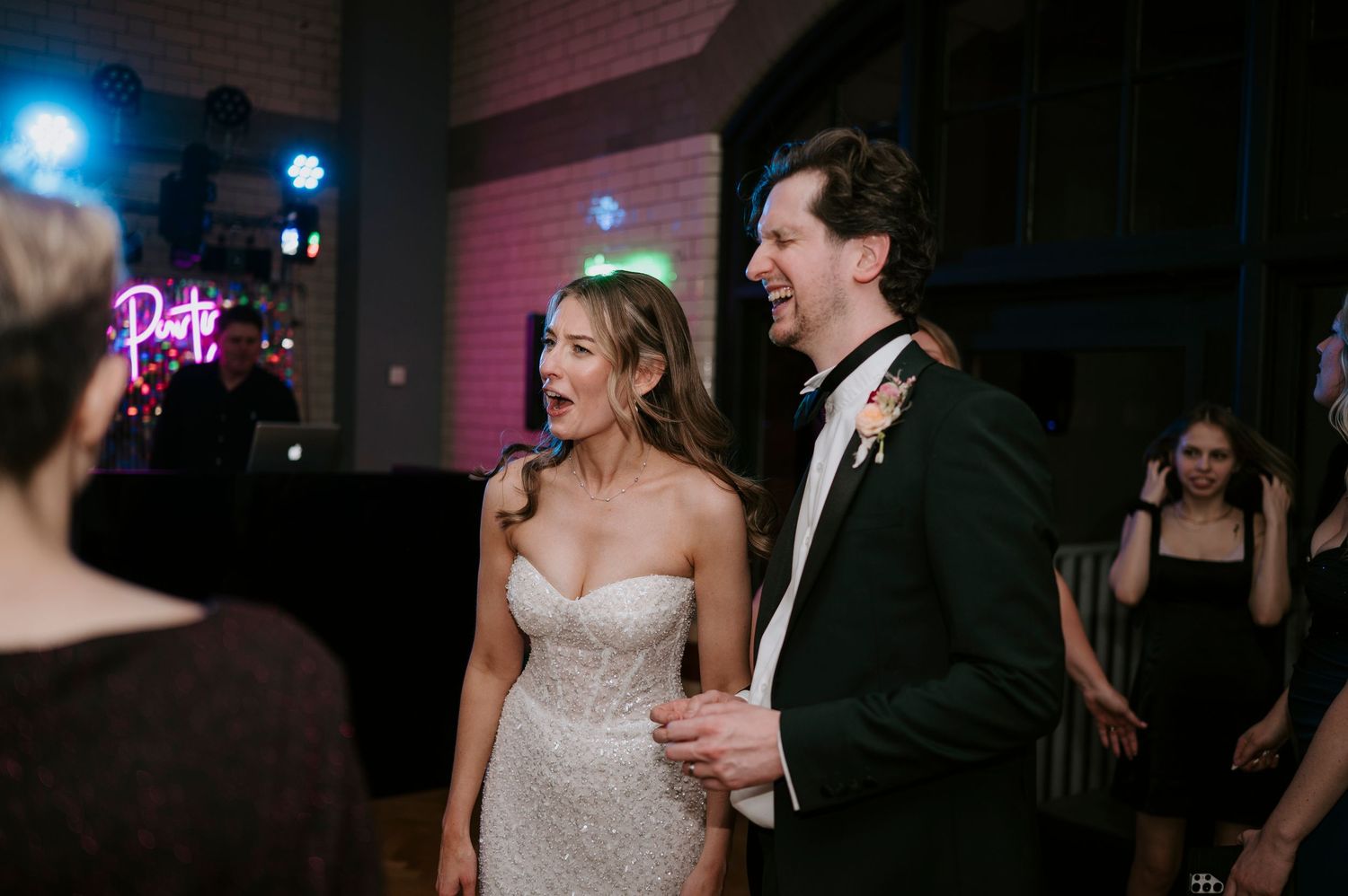 Couples dancing and celebrating under blue and pink neon lighting at a wedding reception.