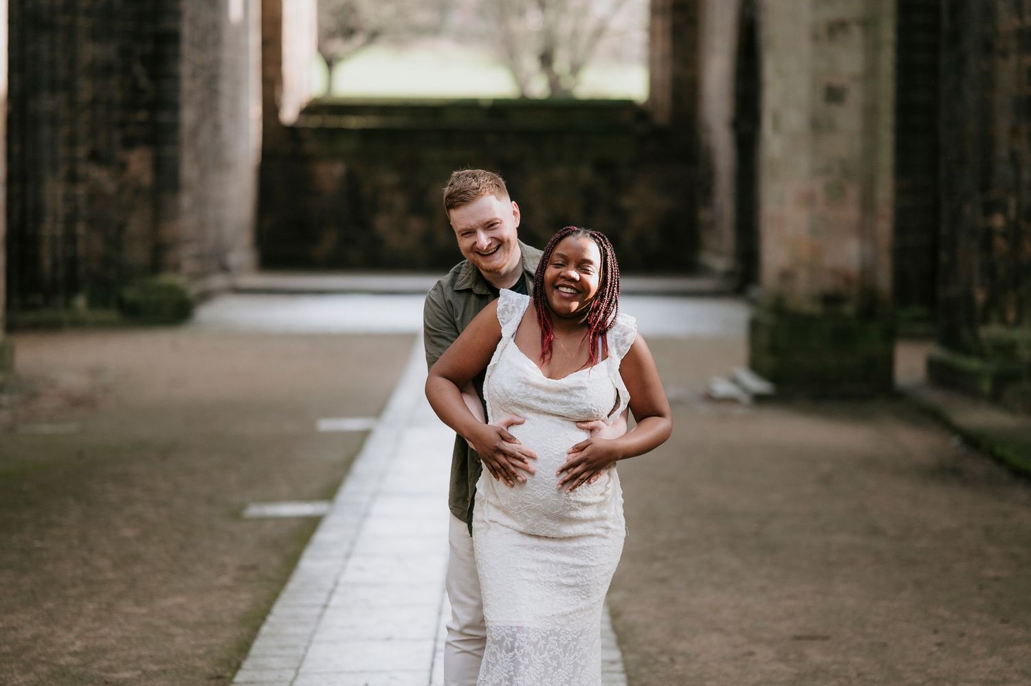 Two people in white wedding attire share a joyful moment together in a rustic stone archway setting.
