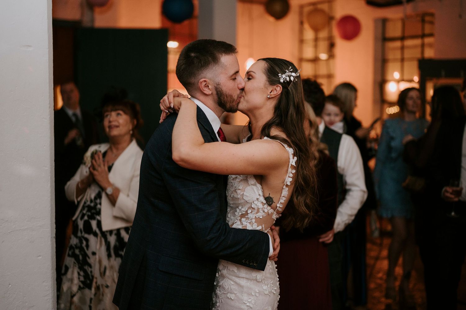 Bride and groom share romantic kiss on dance floor surrounded by wedding guests.
