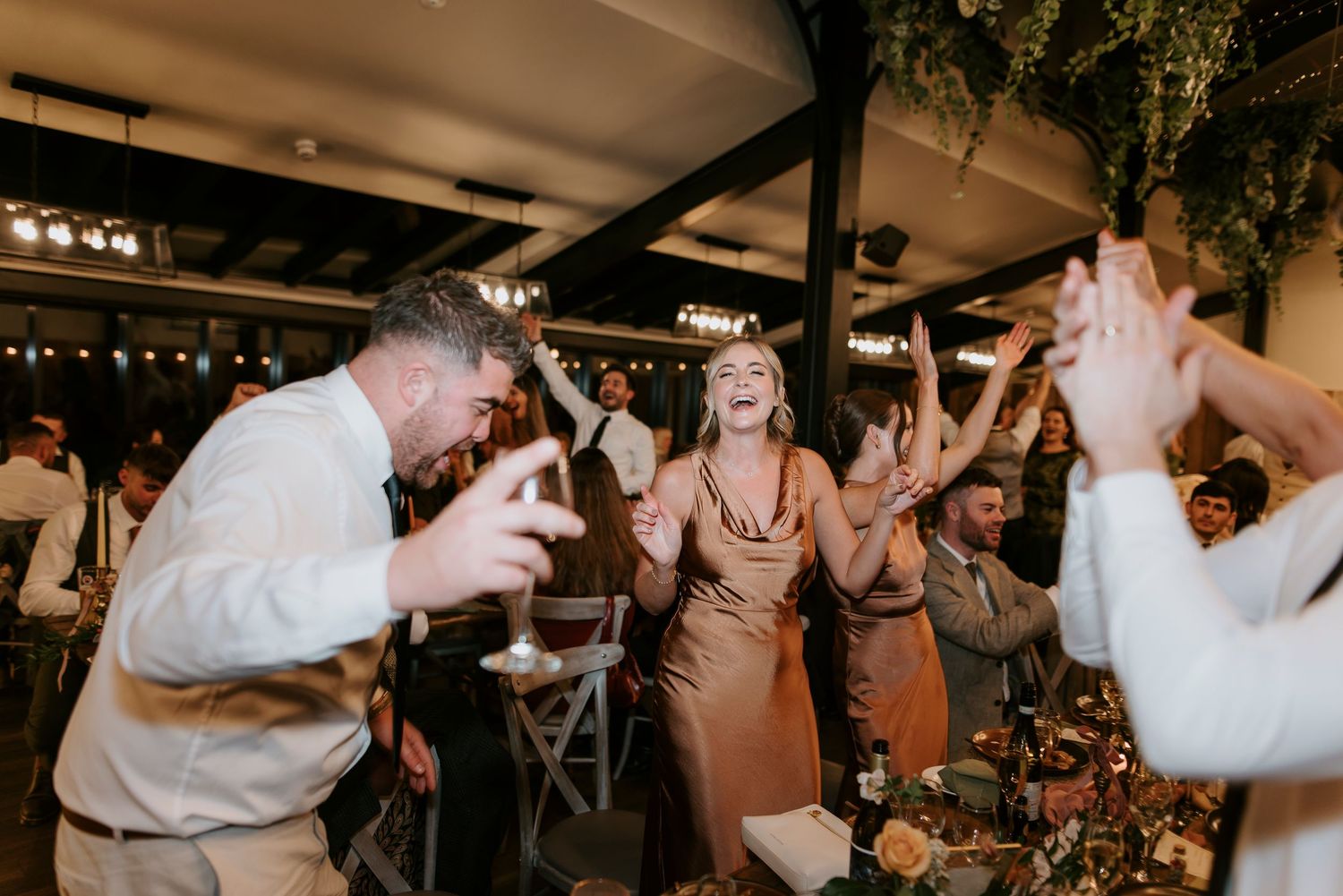 Wedding guests dance and celebrate with raised hands on a lively dance floor at an evening reception.