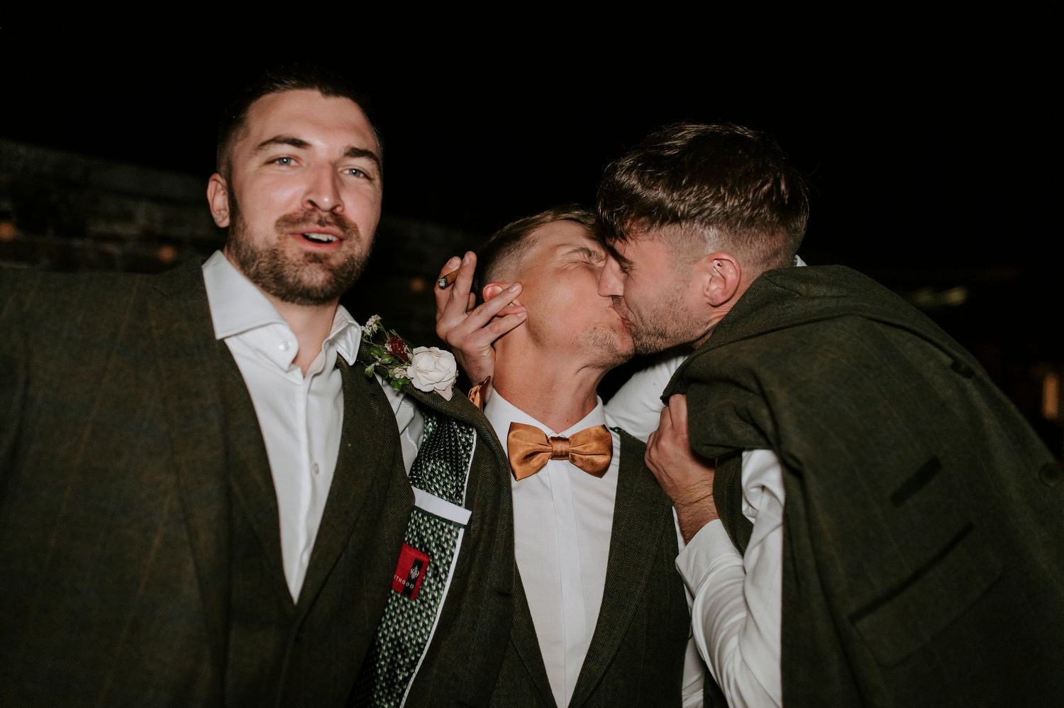 Three people in formal attire sharing a candid moment at a nighttime event.