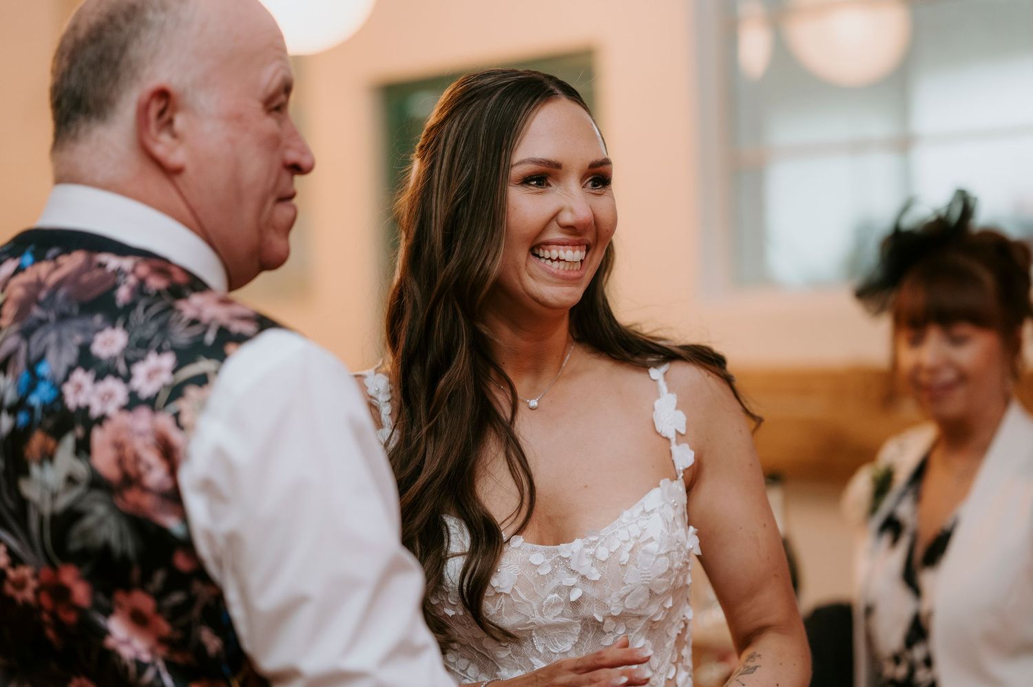 Smiling bride in lace wedding dress laughing joyfully during wedding reception celebration.