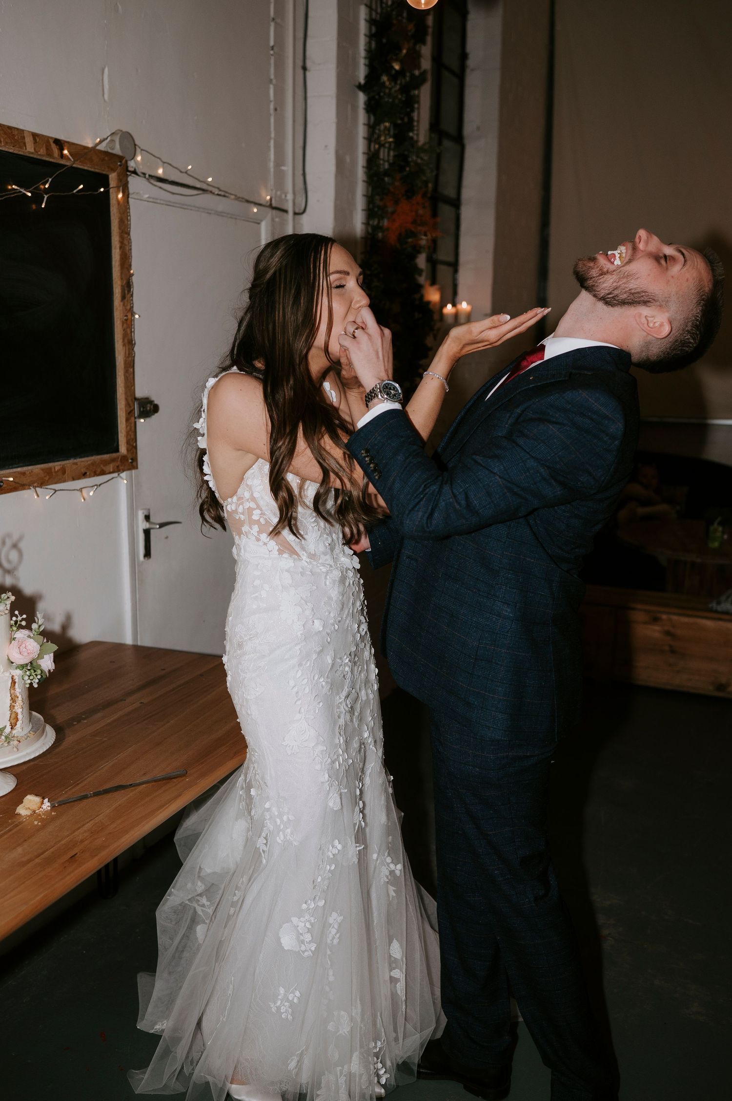 Bride and groom laugh during playful cake smashing moment at their wedding reception.