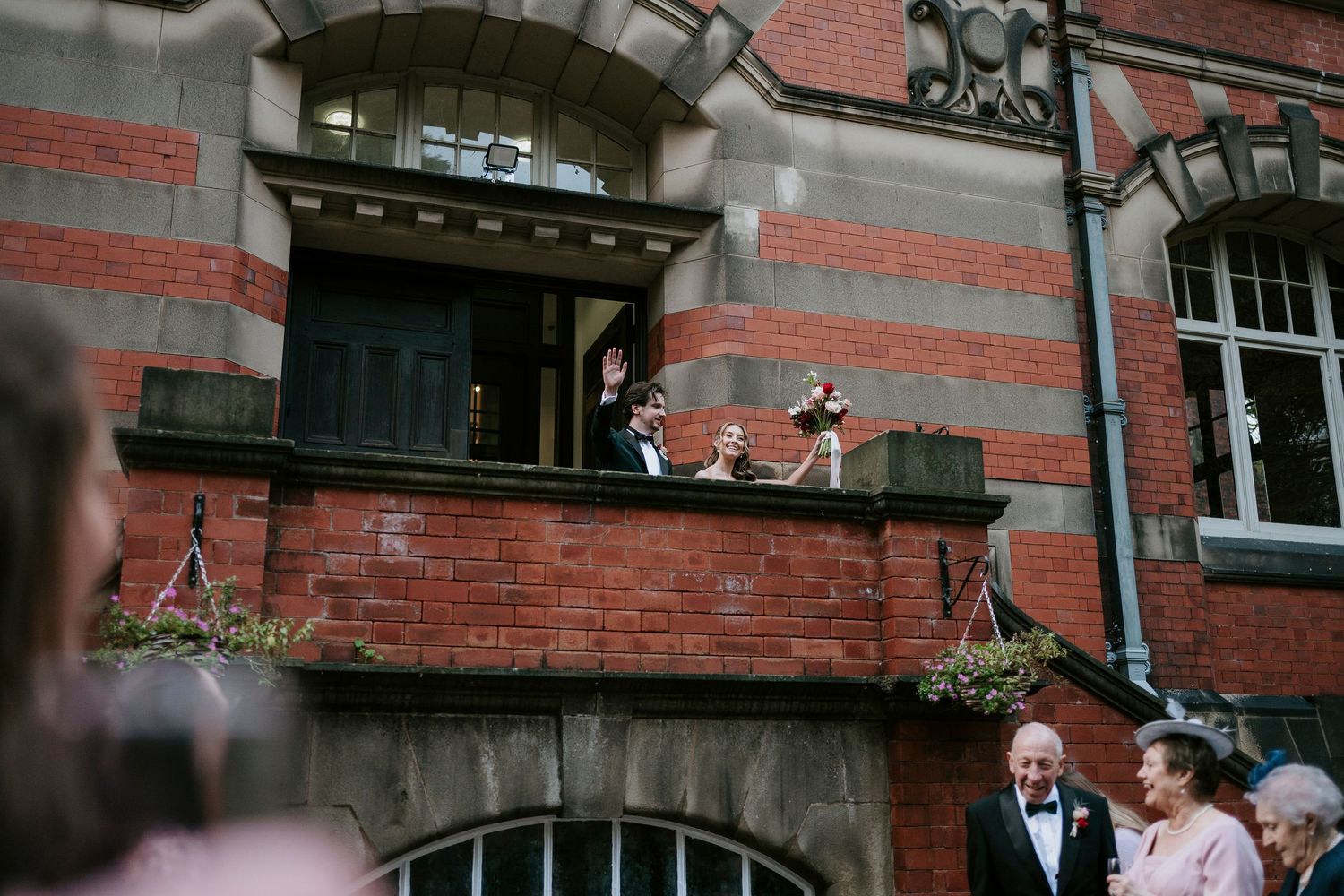 A wedding couple stands in front of a historic red brick building with ornate architectural details.