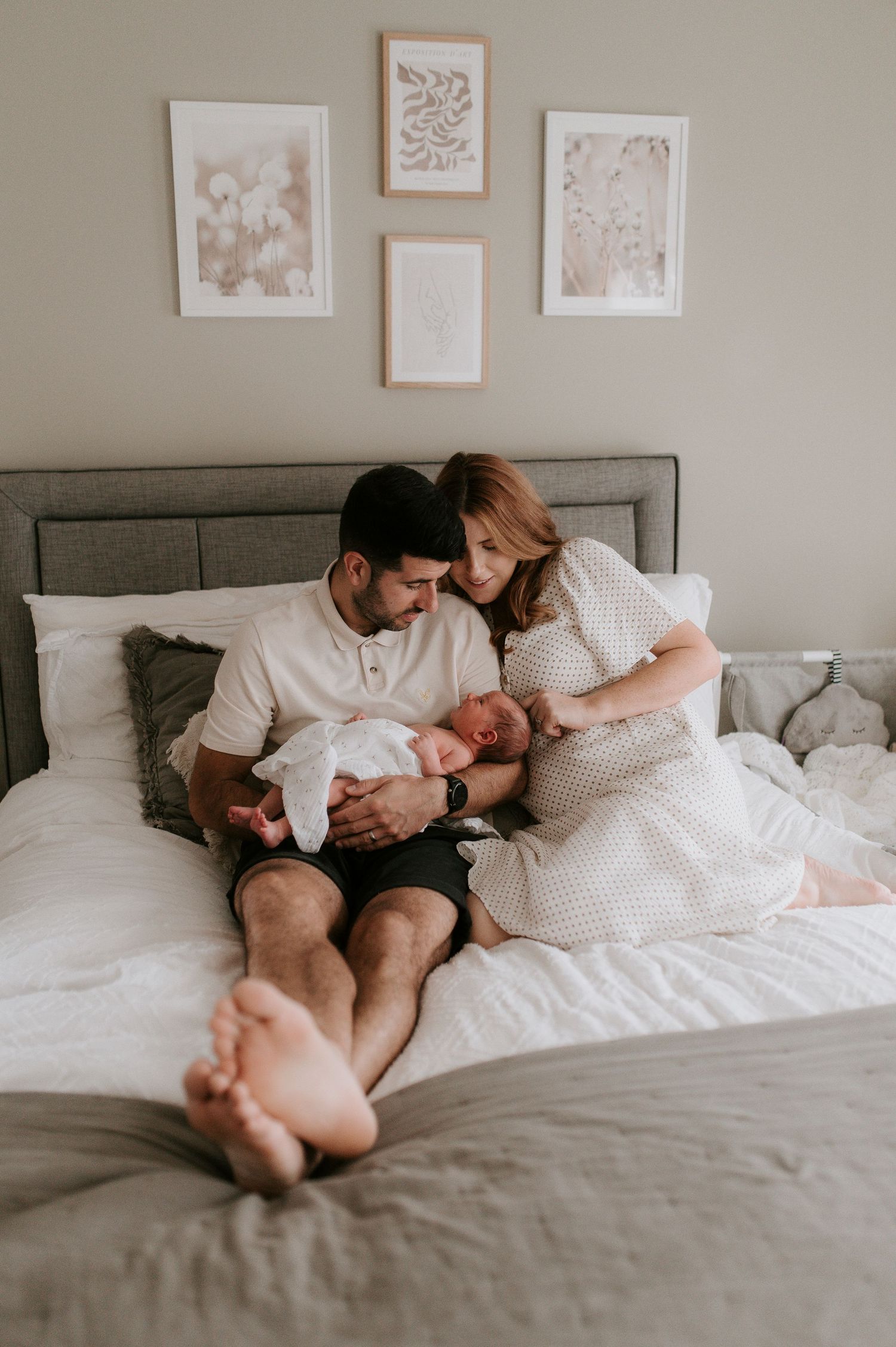 A couple relaxes together on a cozy white bed with framed artwork hanging on the neutral wall above.