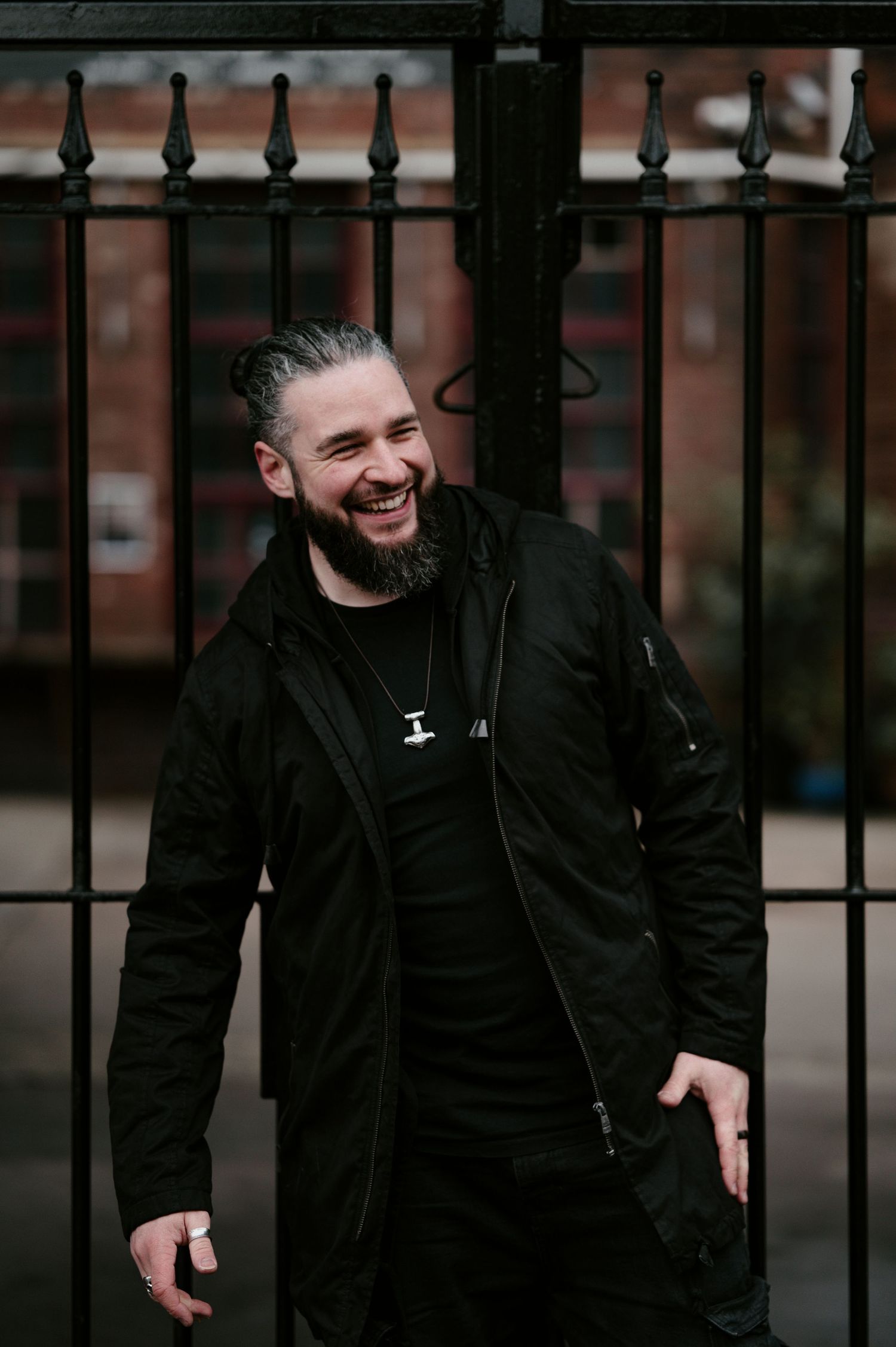 Person in black clothing laughing and posing in front of metal fence.