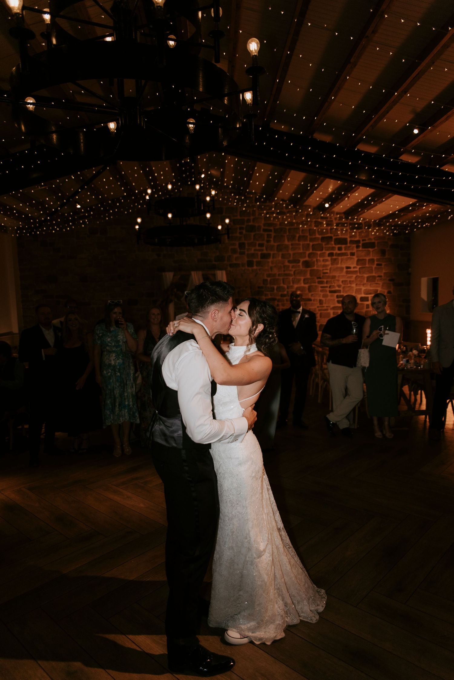 A romantic couple shares their first dance at a rustic wedding reception under twinkling string lights.