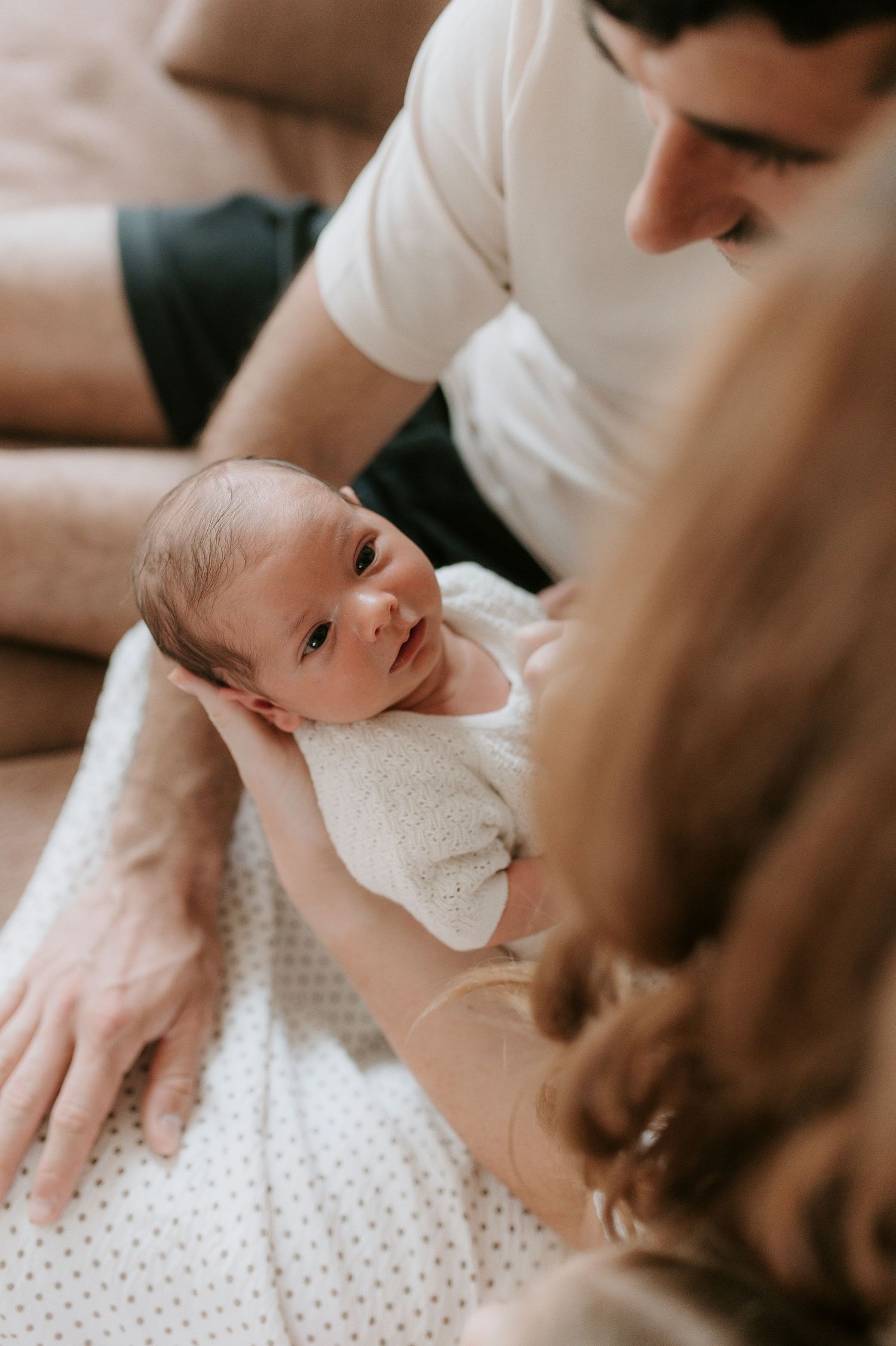 Close-up shots of a baby lying on white polka dot fabric, showing gentle interaction with adult hands.